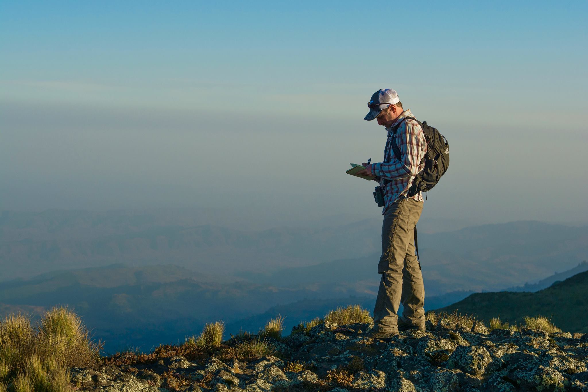 Craig Welch (j’89), senior staff writer at National Geographic, takes notes at dawn at 12,000 feet in the Ethiopian Highlands where he was reporting a story about gelada monkeys. The cliff looks out over northern Africa’s Great Rift Valley. (Photo courtesy of Jeff Kerby, National Geographic)