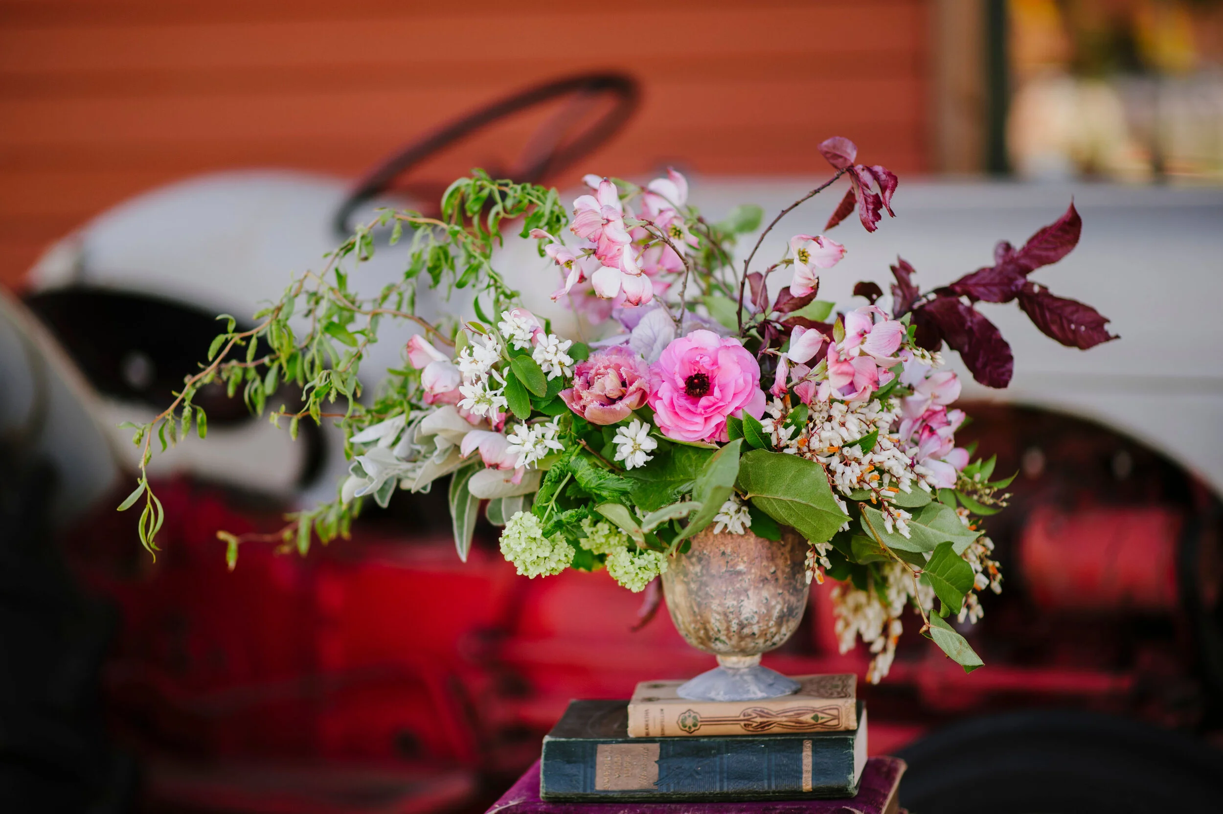 Flower arrangement with pink, white, and purple flowers in a decorative vase, placed on two stacked books.