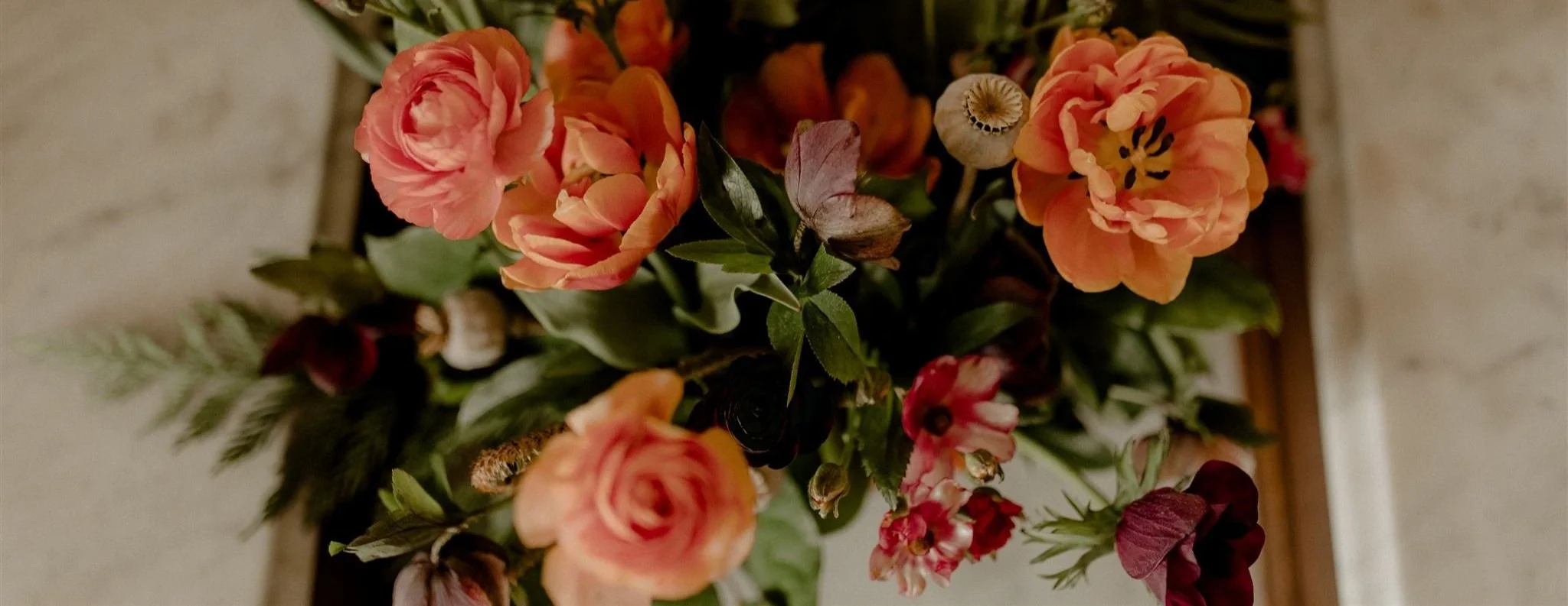 Close-up of a bouquet with various orange, pink, and red flowers and green leaves.