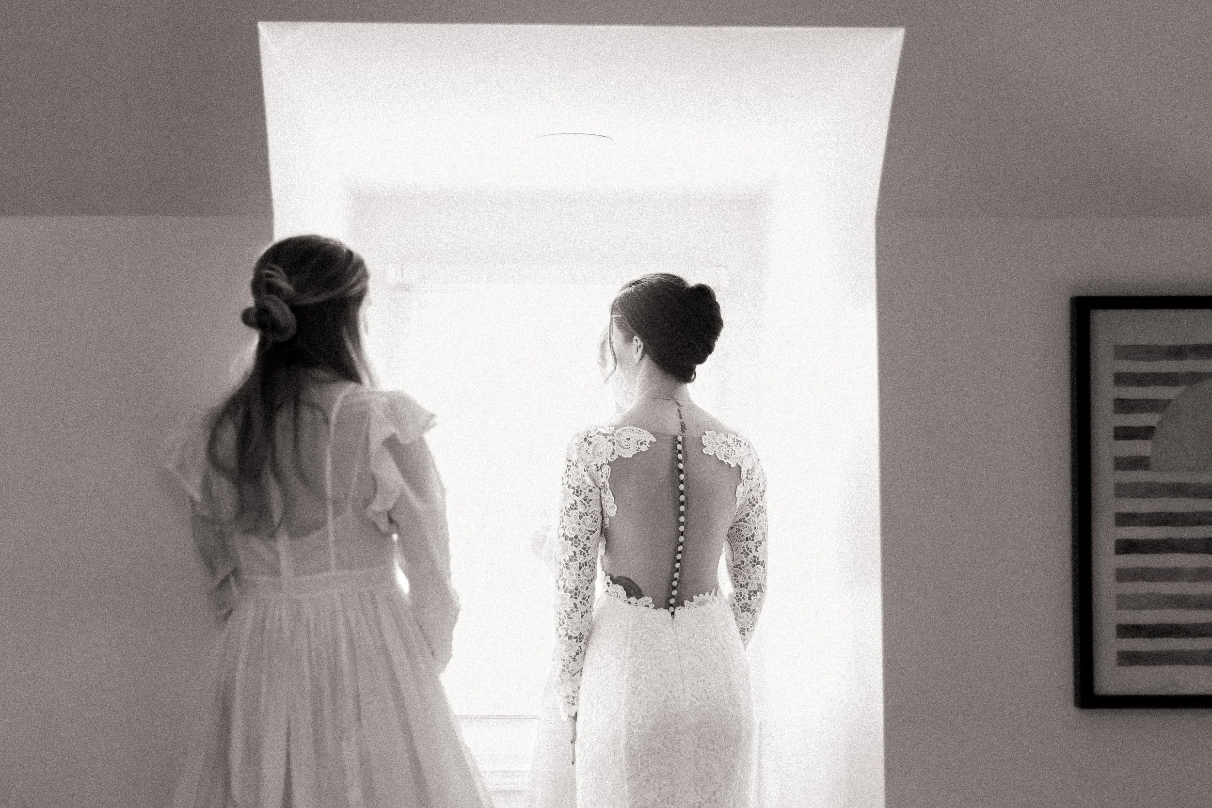 Bride's sister gazes at bride in window light in Olathe.