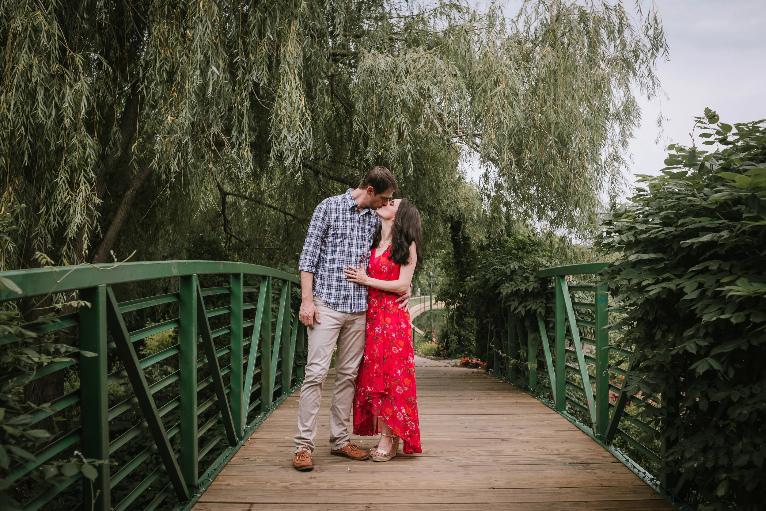 Couple kissing during engagement photos on bridge at Overland Park Arboretum.