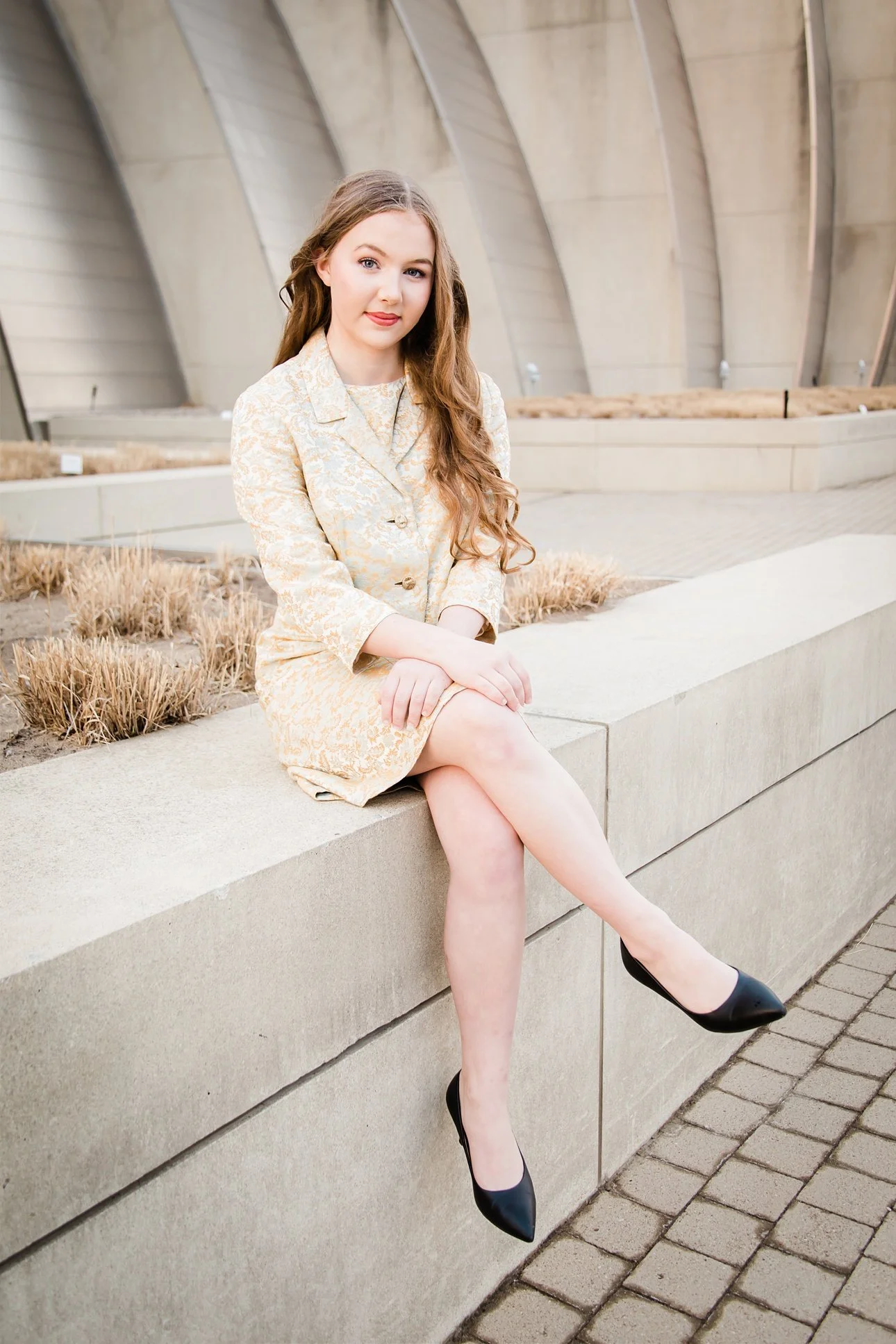 Graduate poses on stone wall in front of the Kauffman Center in Kansas City.