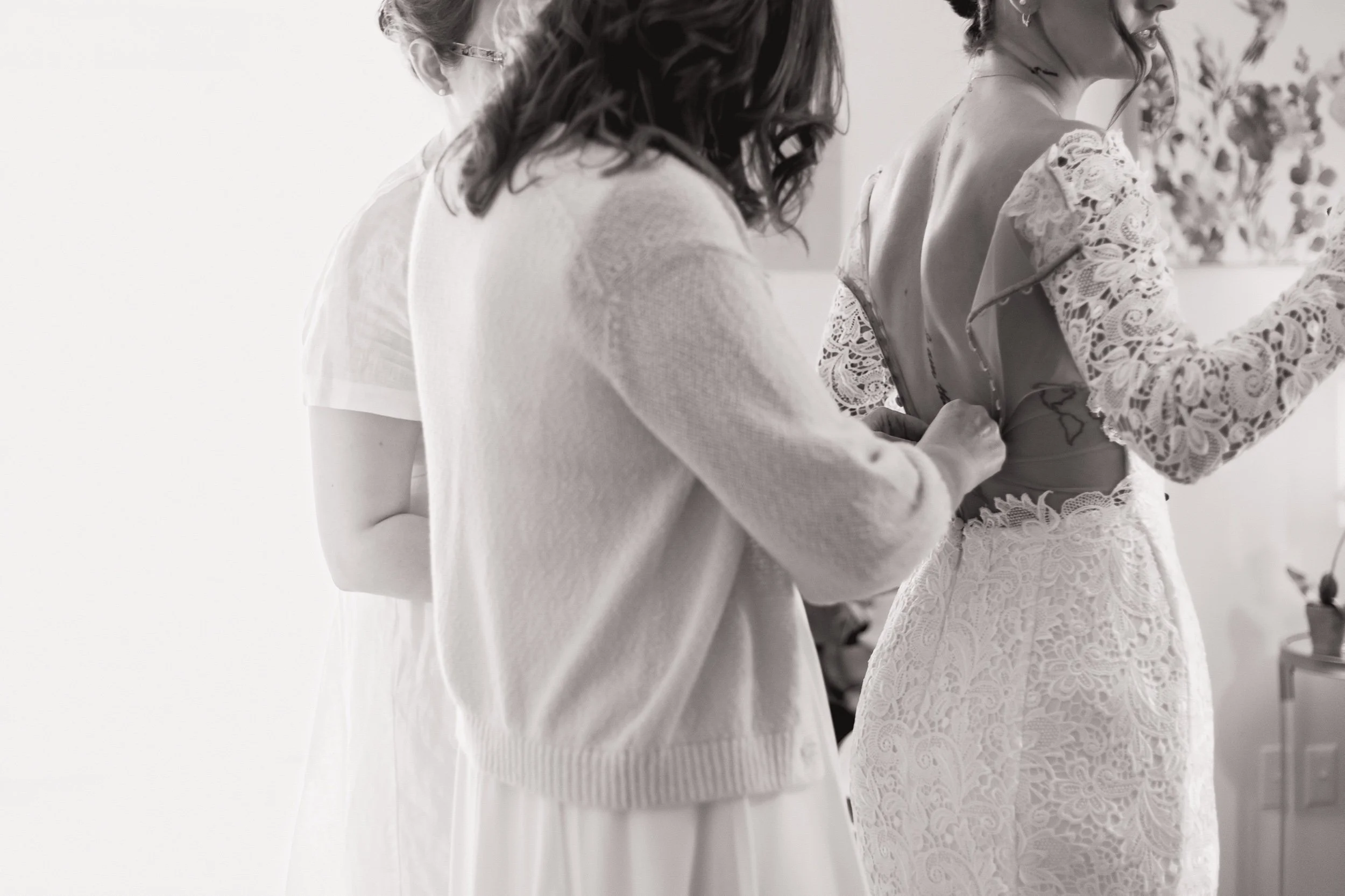 Black and white photo of bride's mother and sister buttoning her dress.