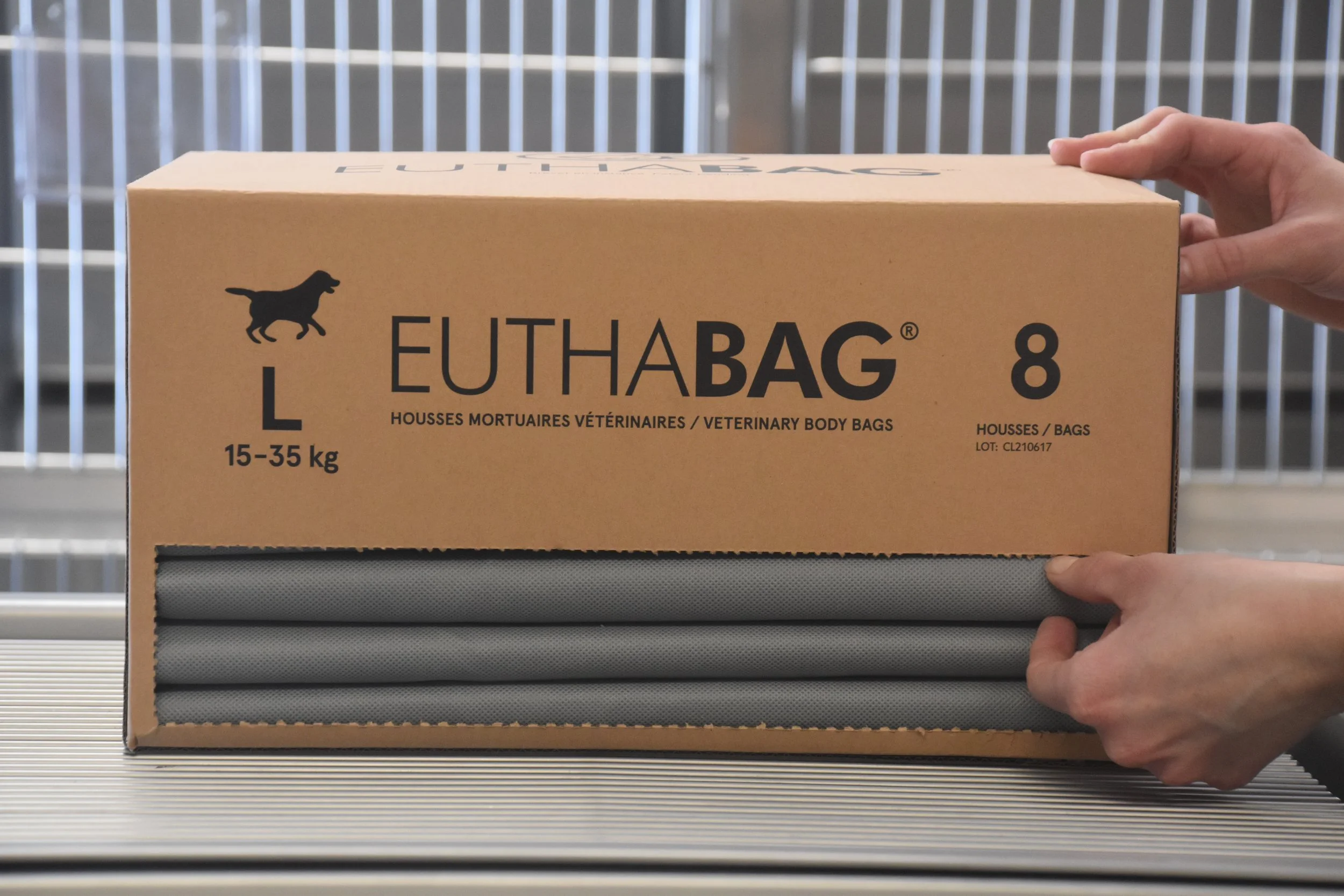 Hands removing a gray EUTHABAG pet body bag from a cardboard dispenser box