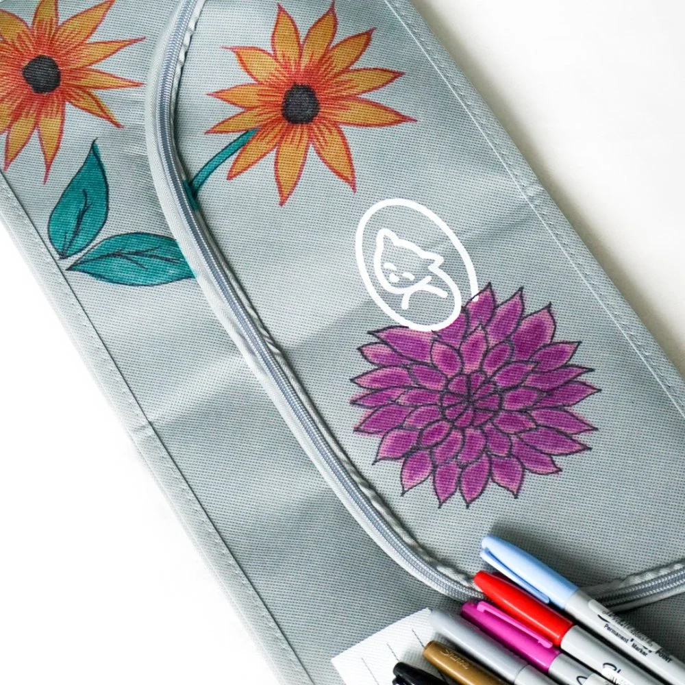 Gray pet body bag decorated with colorful flowers, with markers beside it.
