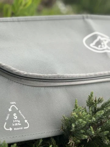 Close-up of a grey EUTHABAG pet body bag featuring a recycling symbol and surrounded by greenery.