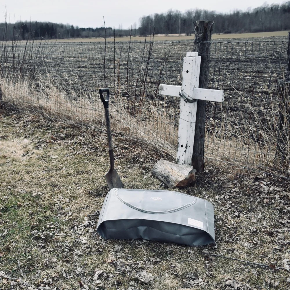 EUTHABAG pet body bag beside a shovel and wooden grave marker in a rural field