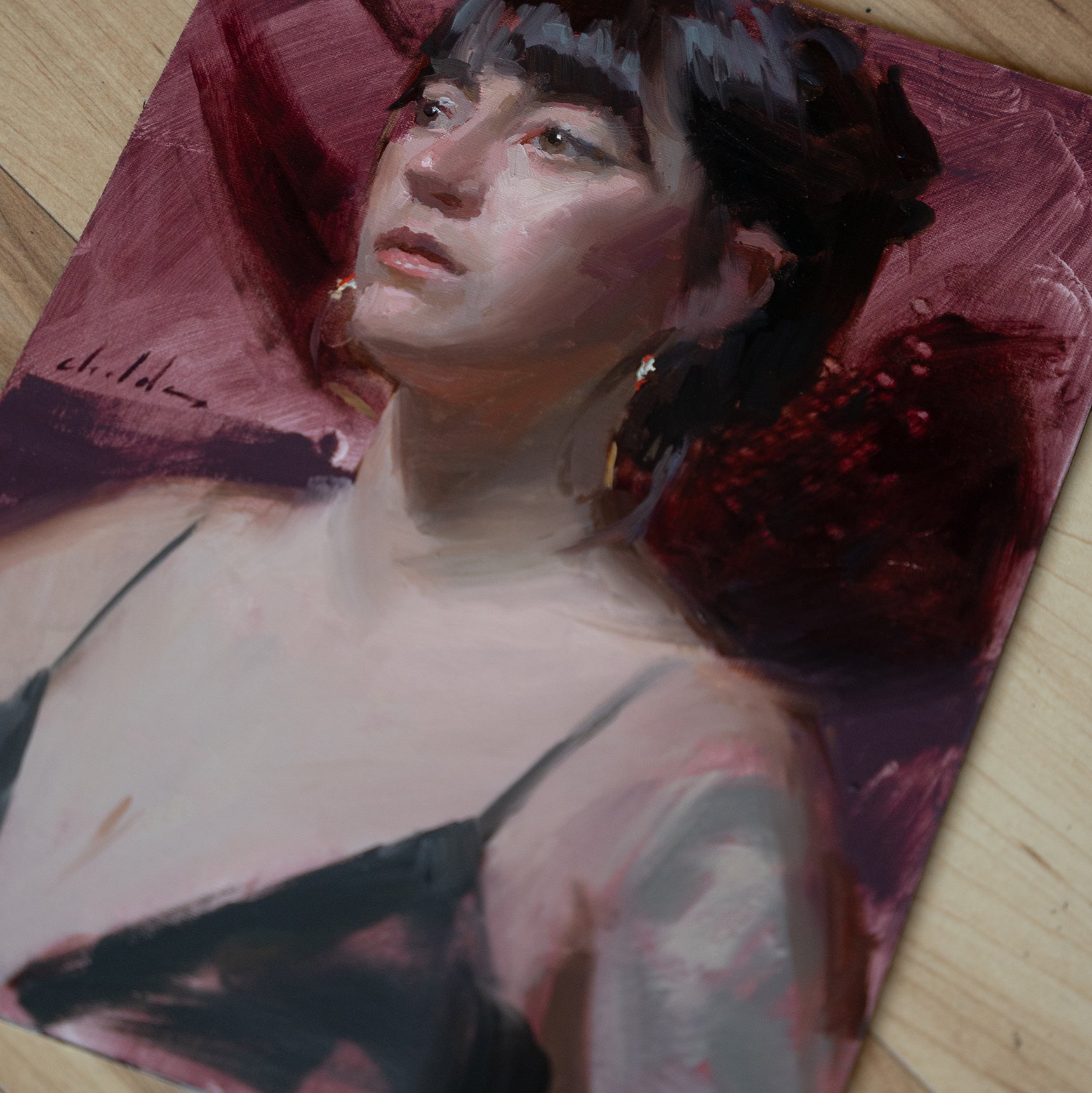 Close-up of a giveaway painting by Casey Childs of a young woman with short dark hair, light skin, and earrings with a red background. the painting is on a wooden floor.
