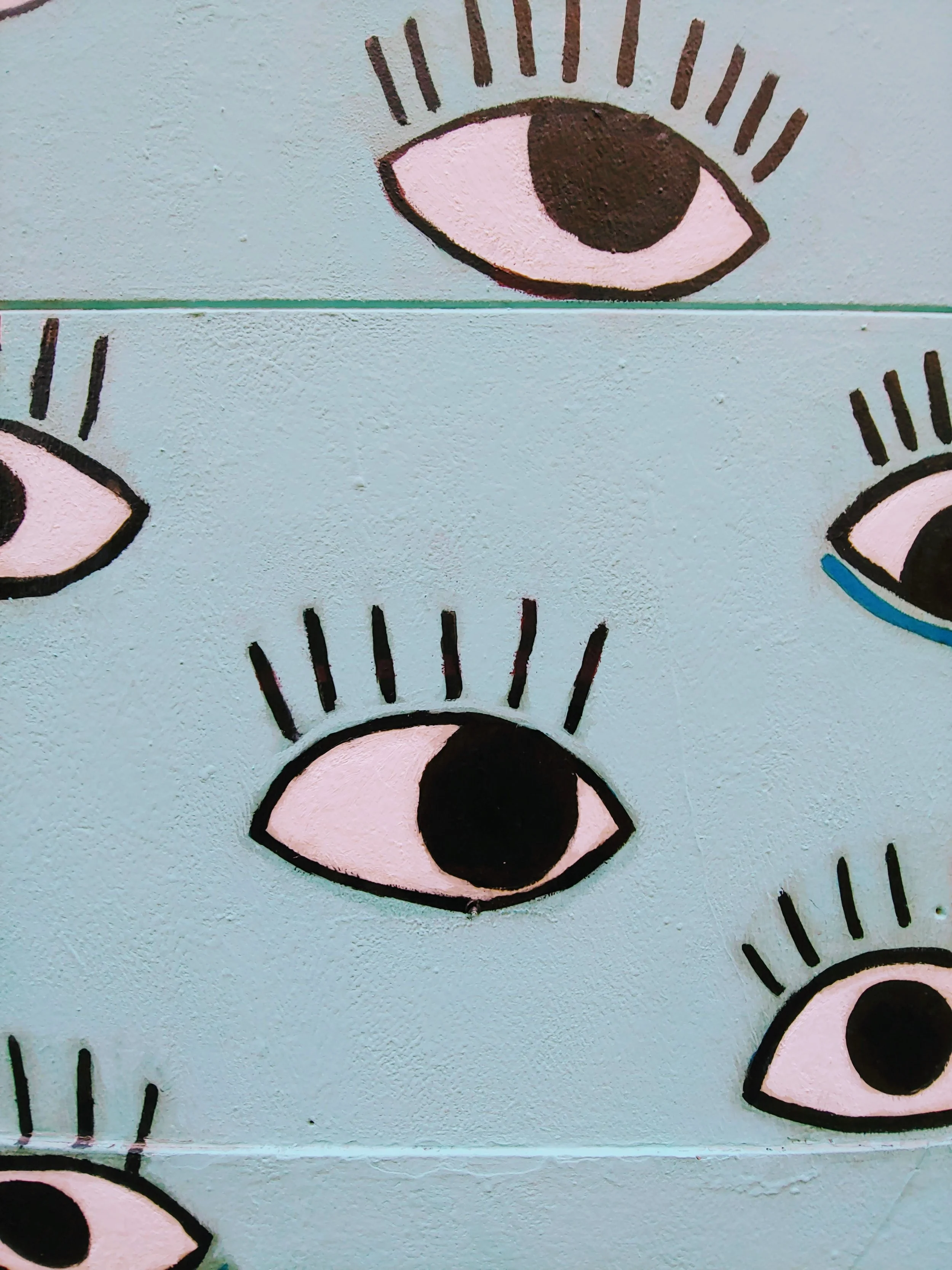 Photo by erika akire on Unsplash . A light blue wall with cartoonish eyes painted on it.