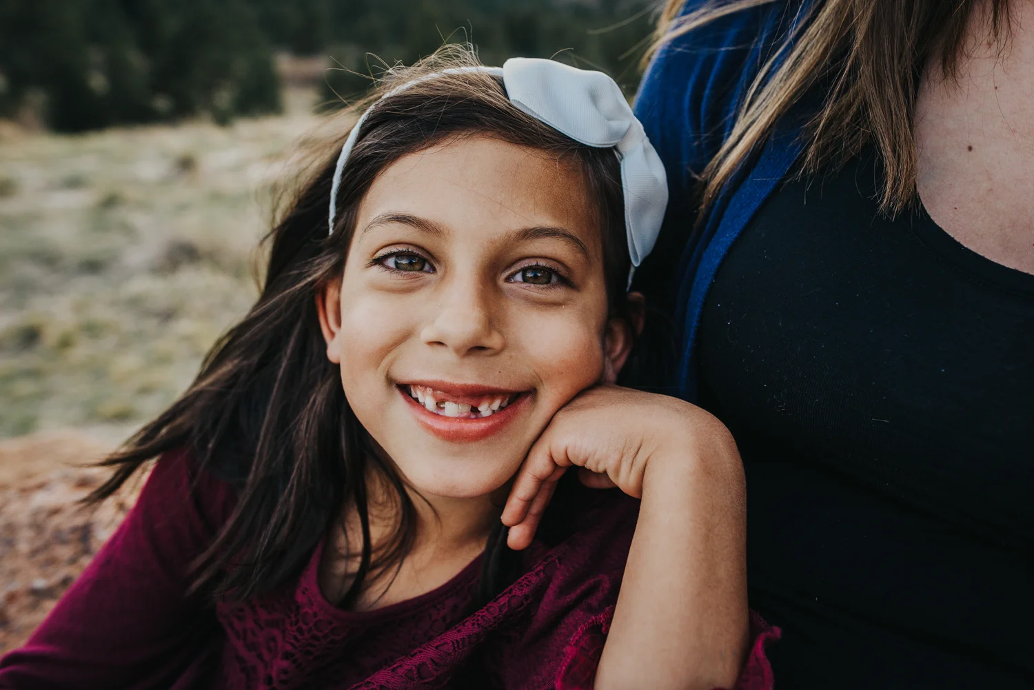 Little girl snuggles with her mother and smiles during family session in Colorado Springs open space.