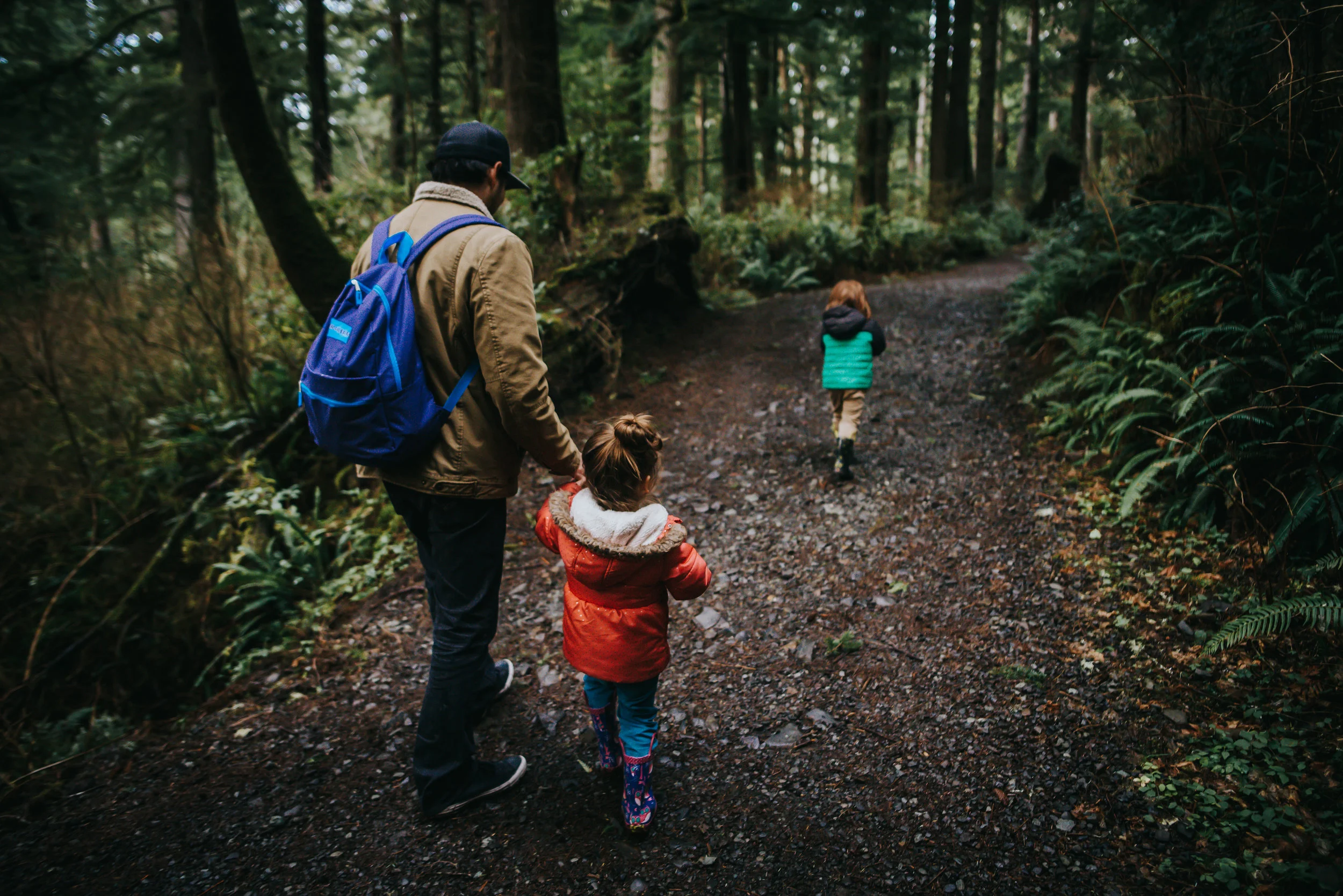A dad walks with his two small children on path in Oregon forest.