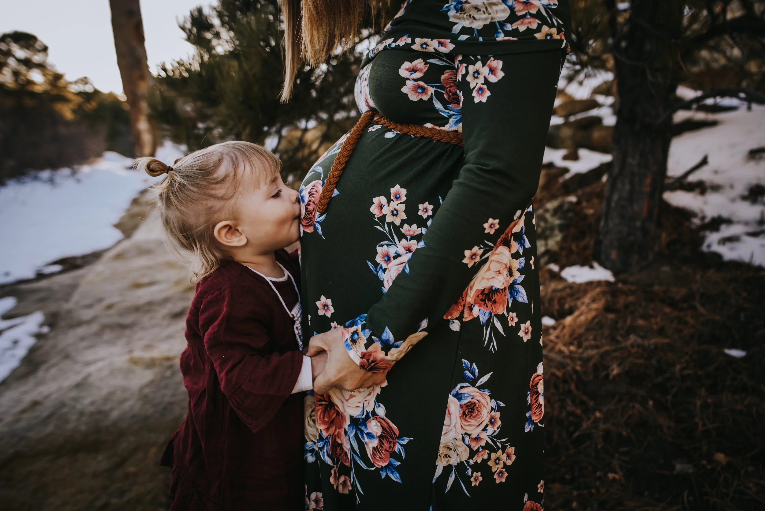 Little girl kisses the pregnant belly of her mother during a maternity family session in Colorado Springs.