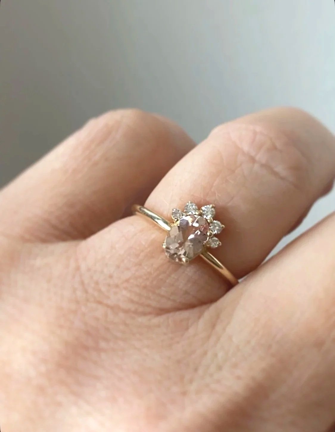 peachy pink oval morganite with little crown of Canadian diamonds claw set in 14k yellow gold narrow rounded band on hand through finger view Kim Drosdick Jewellery Toronto