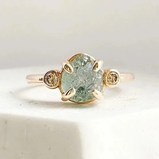 round Montana minty blue green claw set engagement ring with side bezel set champagne diamonds 14k yellow gold on prop dish Kim Drosdick Jewellery Toronto