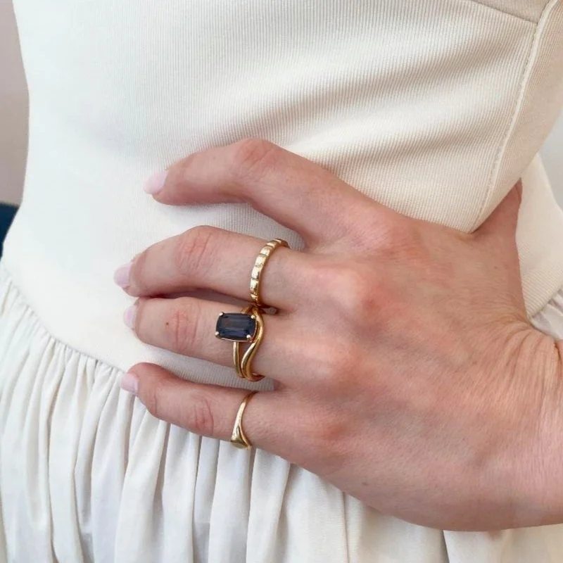 dark blue cushion cut spinel solitaire engagement ring 14ky recycled gold in a stack on a woman in a cream dress Kim Drosdick Toronto