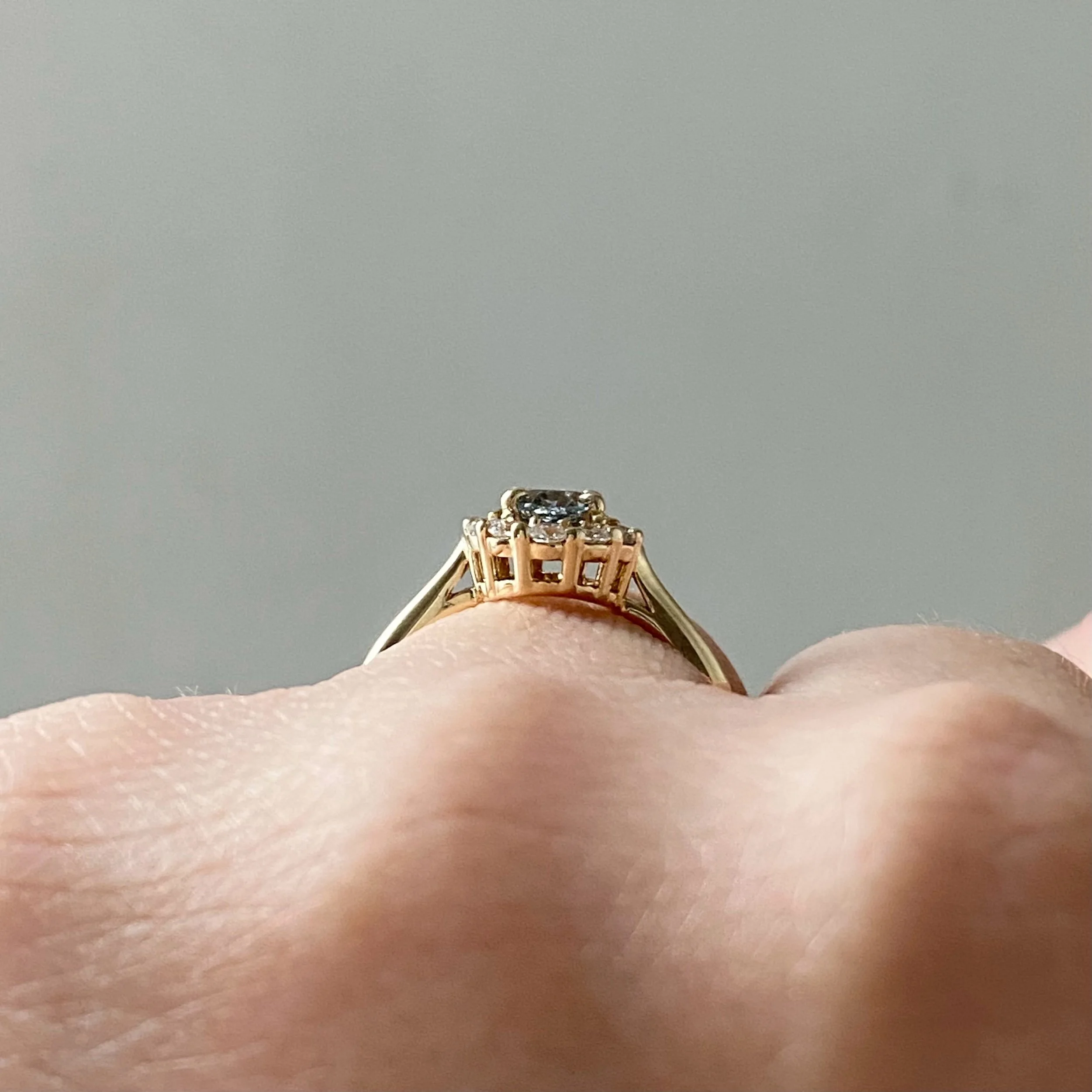 oval blue green spinel claw set in a Canadian diamond halo engagement ring 14k yellow gold through finger view on hand Kim Drosdick Jewellery