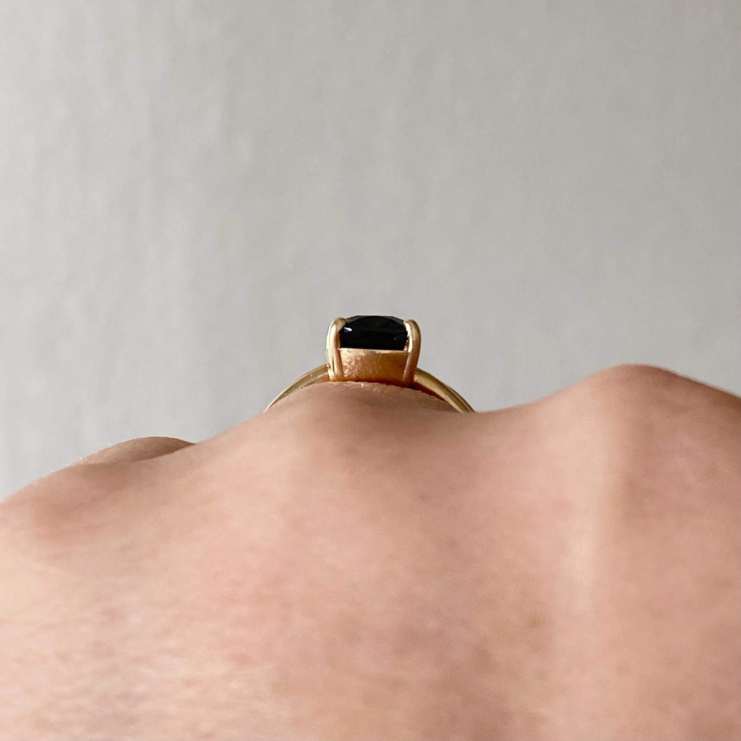 elongated cushion dark blue purple spinel claw set solitaire 14k yellow gold engagement ring on hand through finger view Kim Drosdick Jewellery Toronto