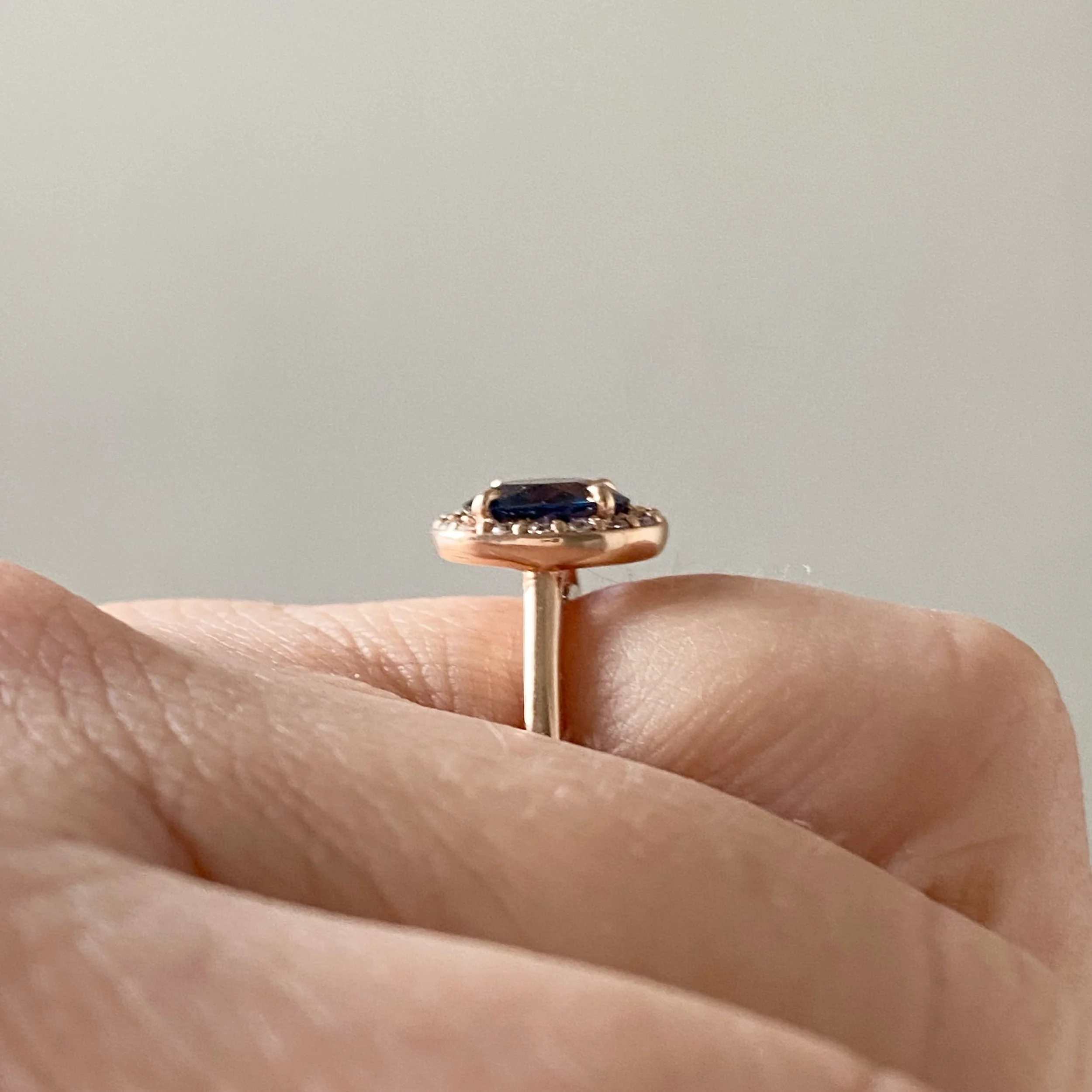 gorgeous oval blue spinel centre stone Canadian diamond halo engagement ring 14k rose gold on hand side view Kim Drosdick Jewellery