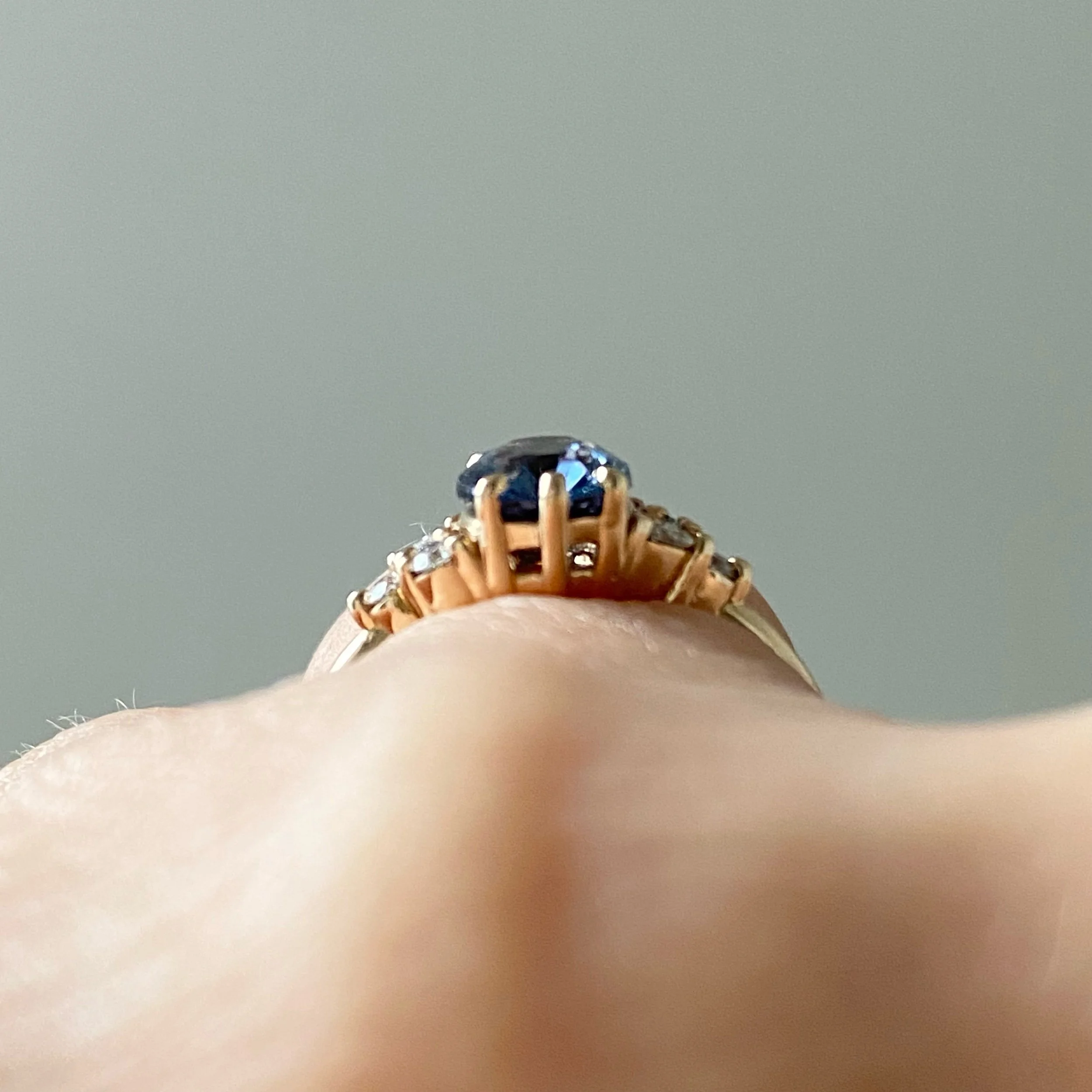 oval blue violet spinel diamond accents mirrored side clusters 14k yellow gold engagement ring through finger view Kim Drosdick Jewellery