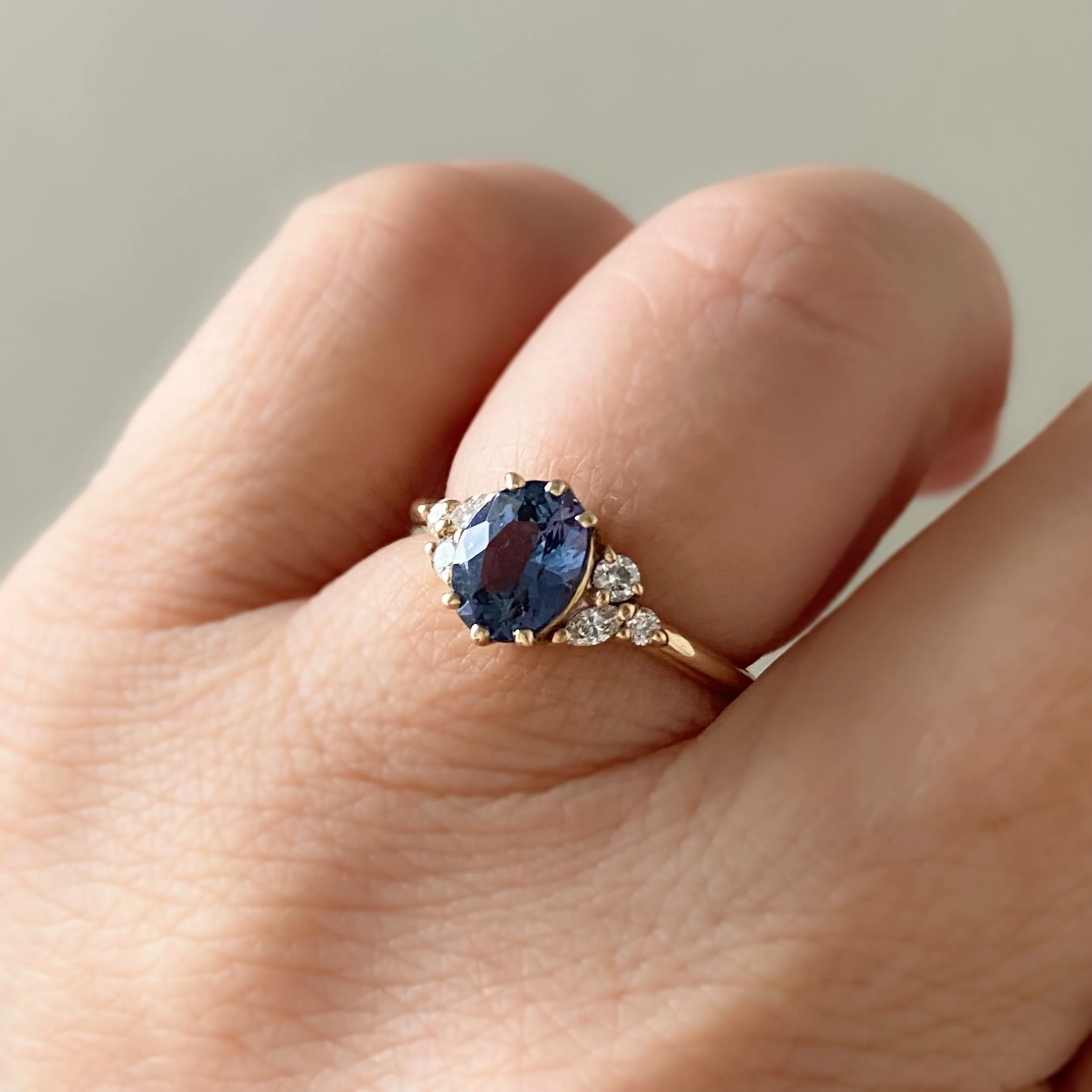 oval blue violet spinel diamond accents mirrored side clusters 14k yellow gold engagement ring on hand Kim Drosdick Jewellery