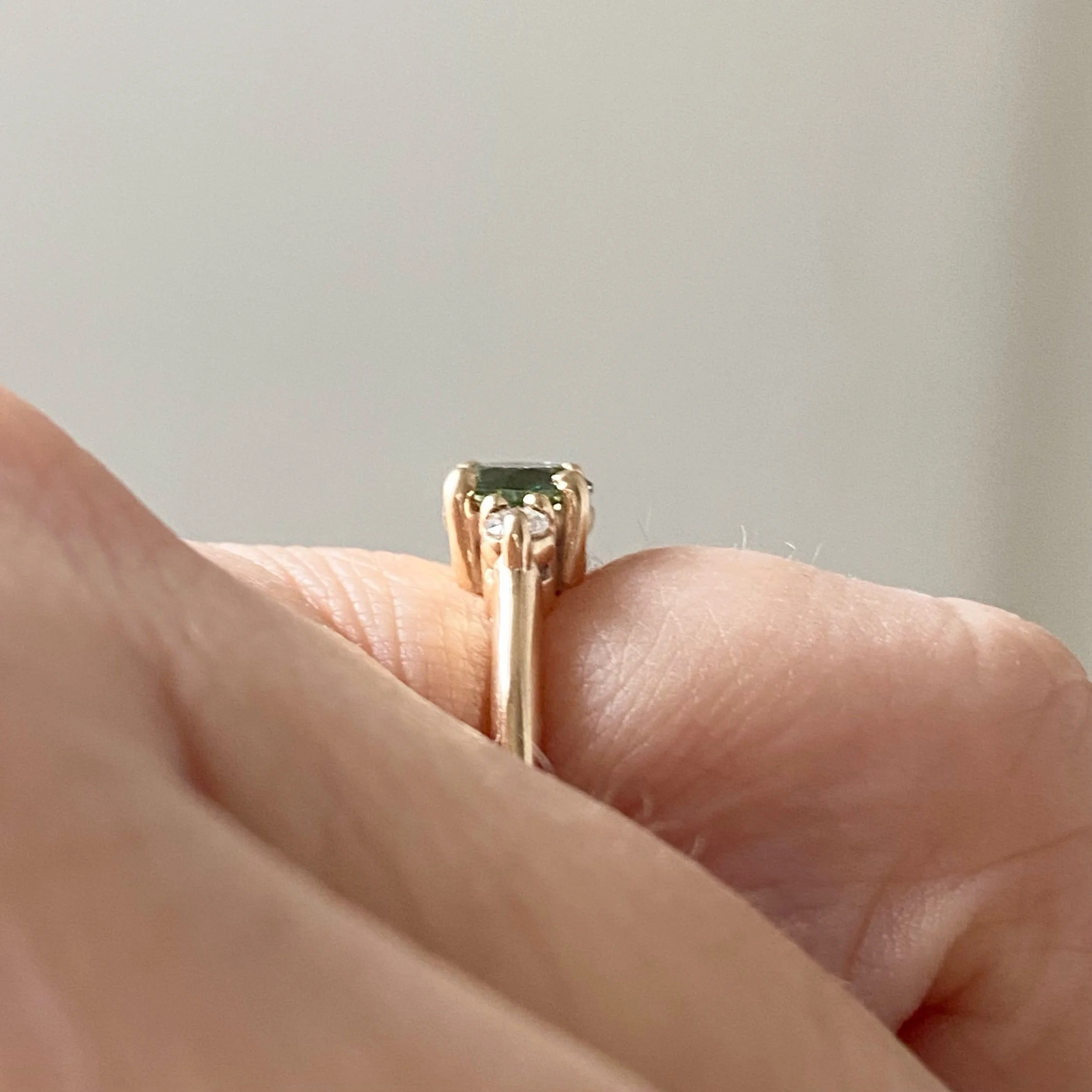 round green sapphire engagement ring with round Canadian side diamonds claw setting 3 stone 14k yellow gold ring side profile on hand Kim Drosdick Jewellery