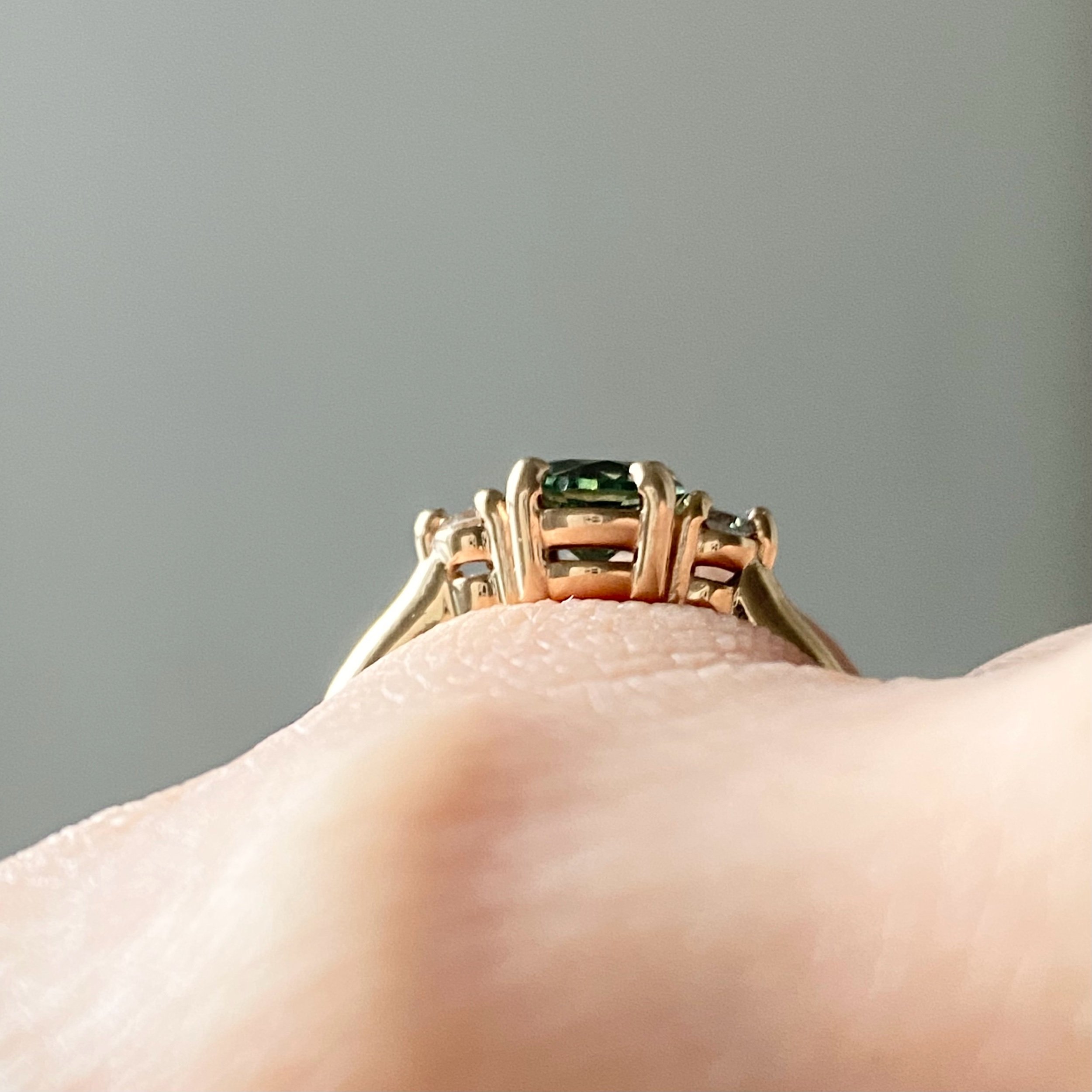 round green sapphire engagement ring with round Canadian side diamonds claw setting 3 stone 14k yellow gold ring through finger view on hand Kim Drosdick Jewellery