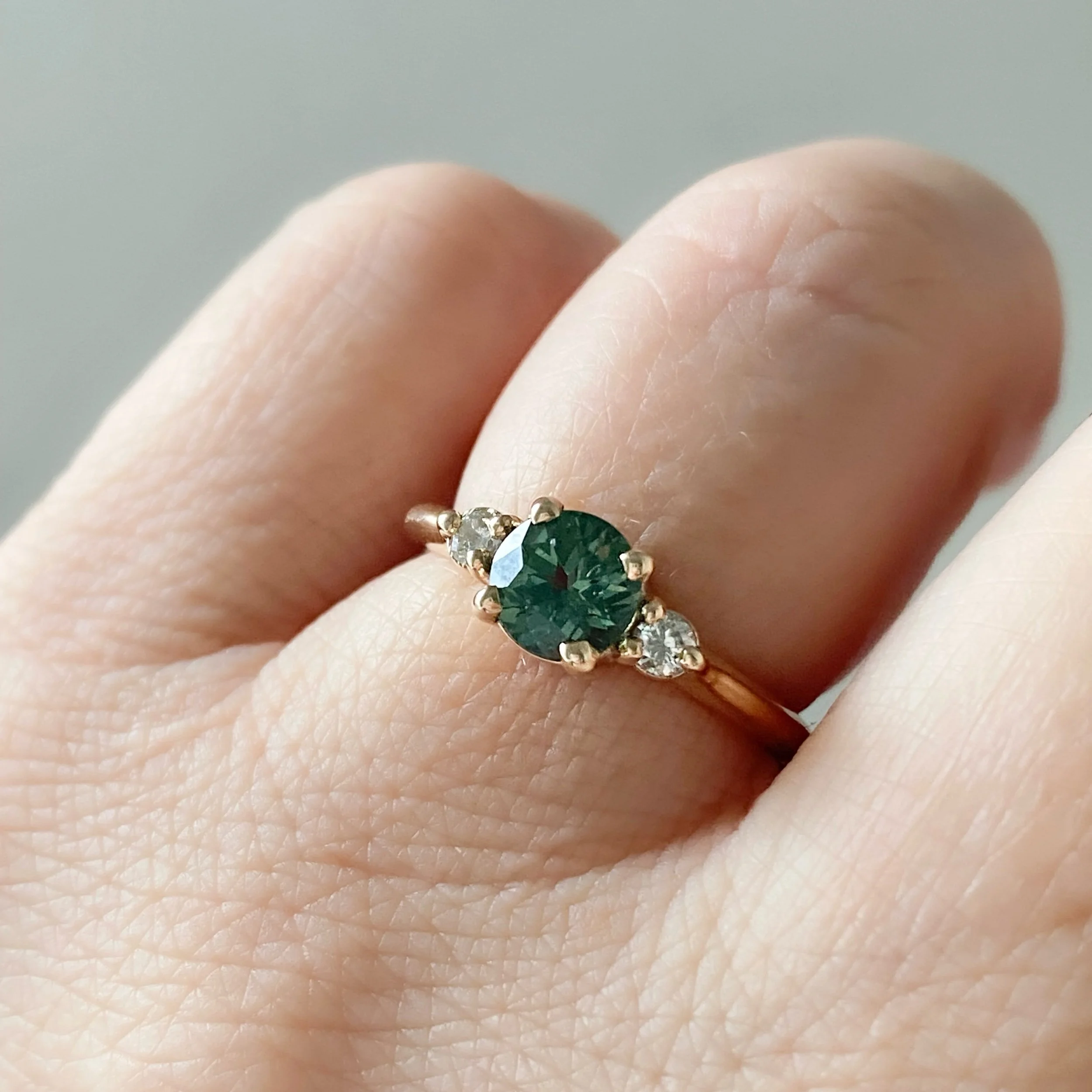 round green sapphire engagement ring with round Canadian side diamonds claw setting 3 stone 14k yellow gold ring on hand Kim Drosdick Jewellery