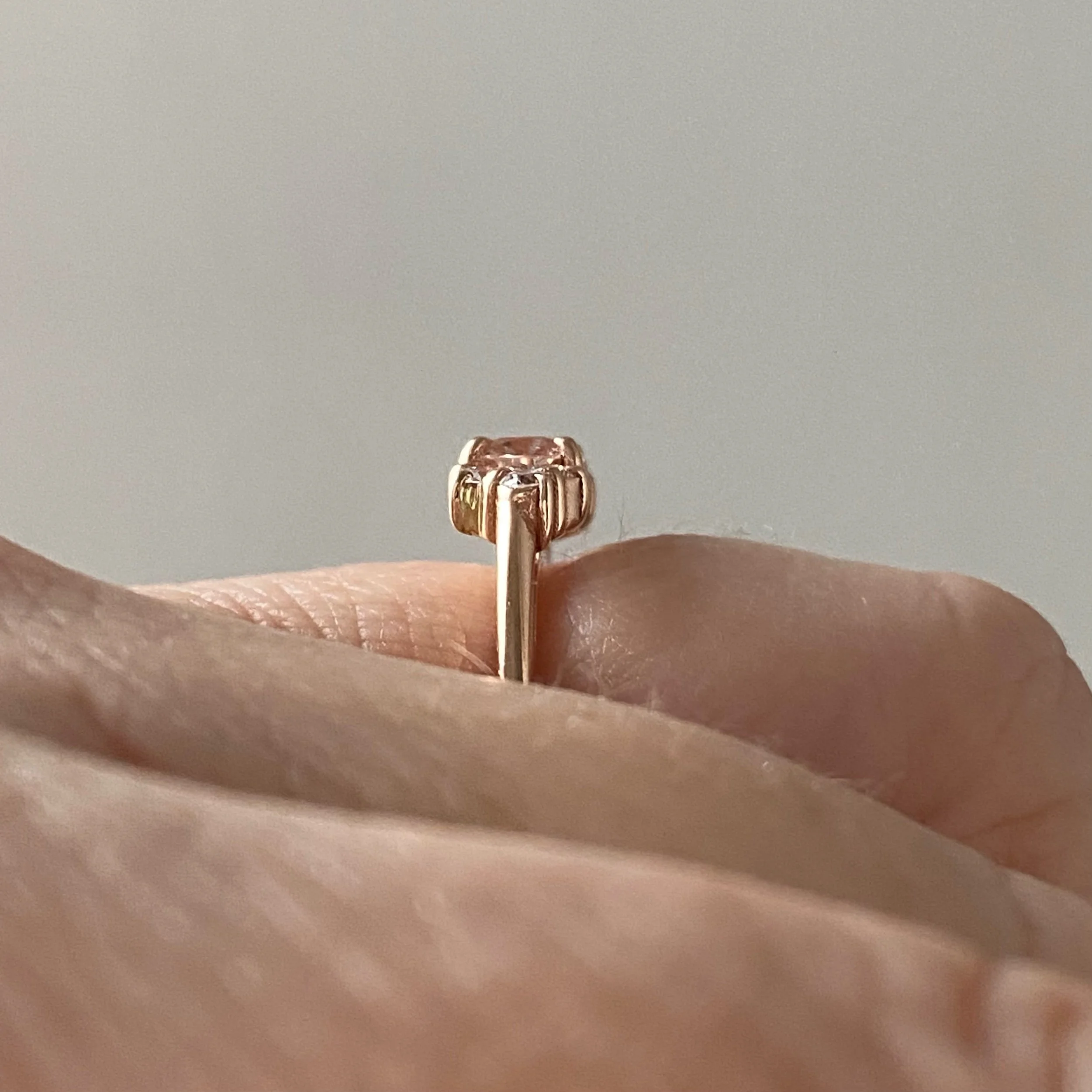 east west claw set oval morganite with mixed size round mirrored canadian diamond clusters shown on hand and raised to allows future flush wedding ring 14k rose gold Kim Drosdick Jewellery Toronto