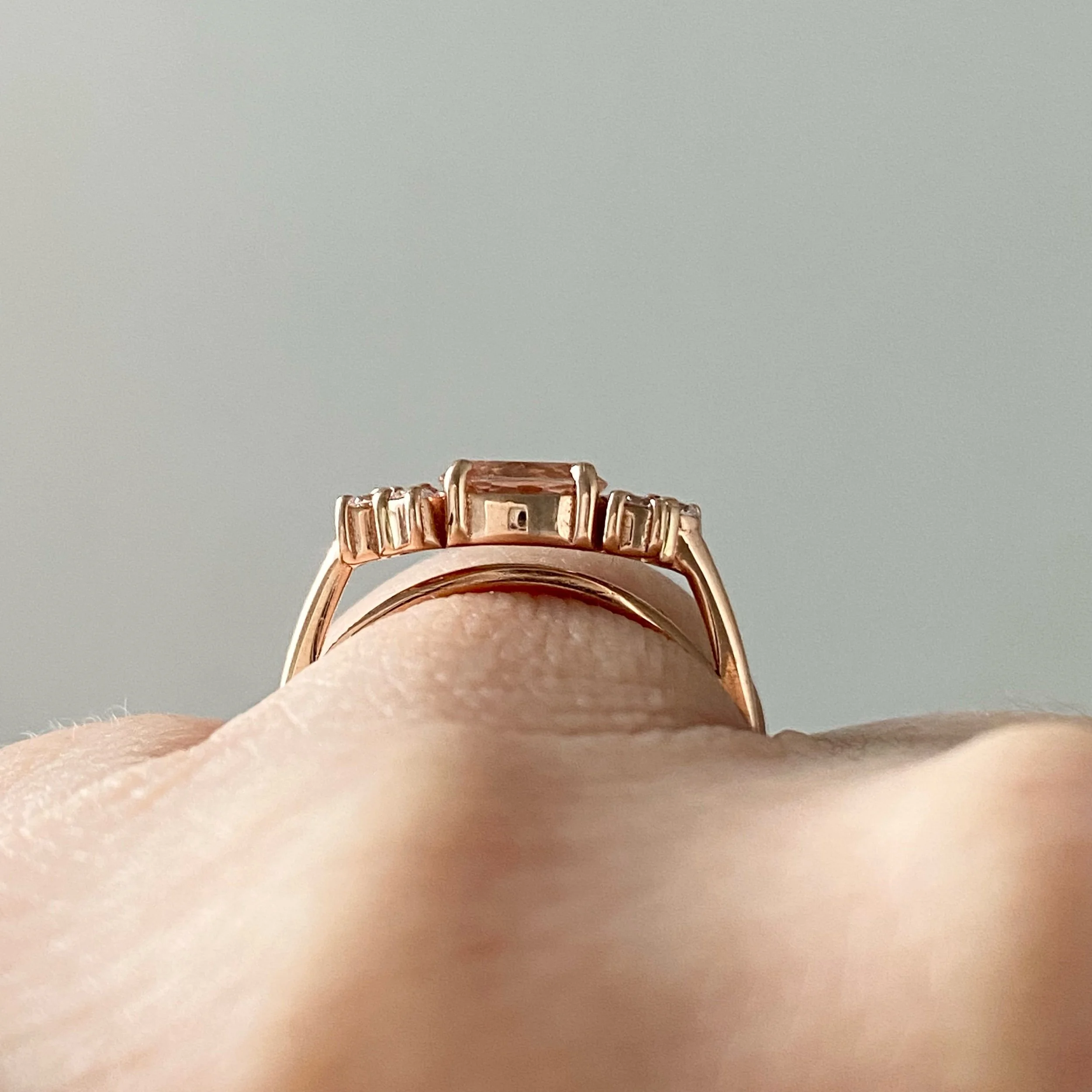 east west claw set oval morganite with mixed size round mirrored canadian diamond clusters shown on hand and raised to allows future flush wedding ring 14k rose gold Kim Drosdick Jewellery Toronto