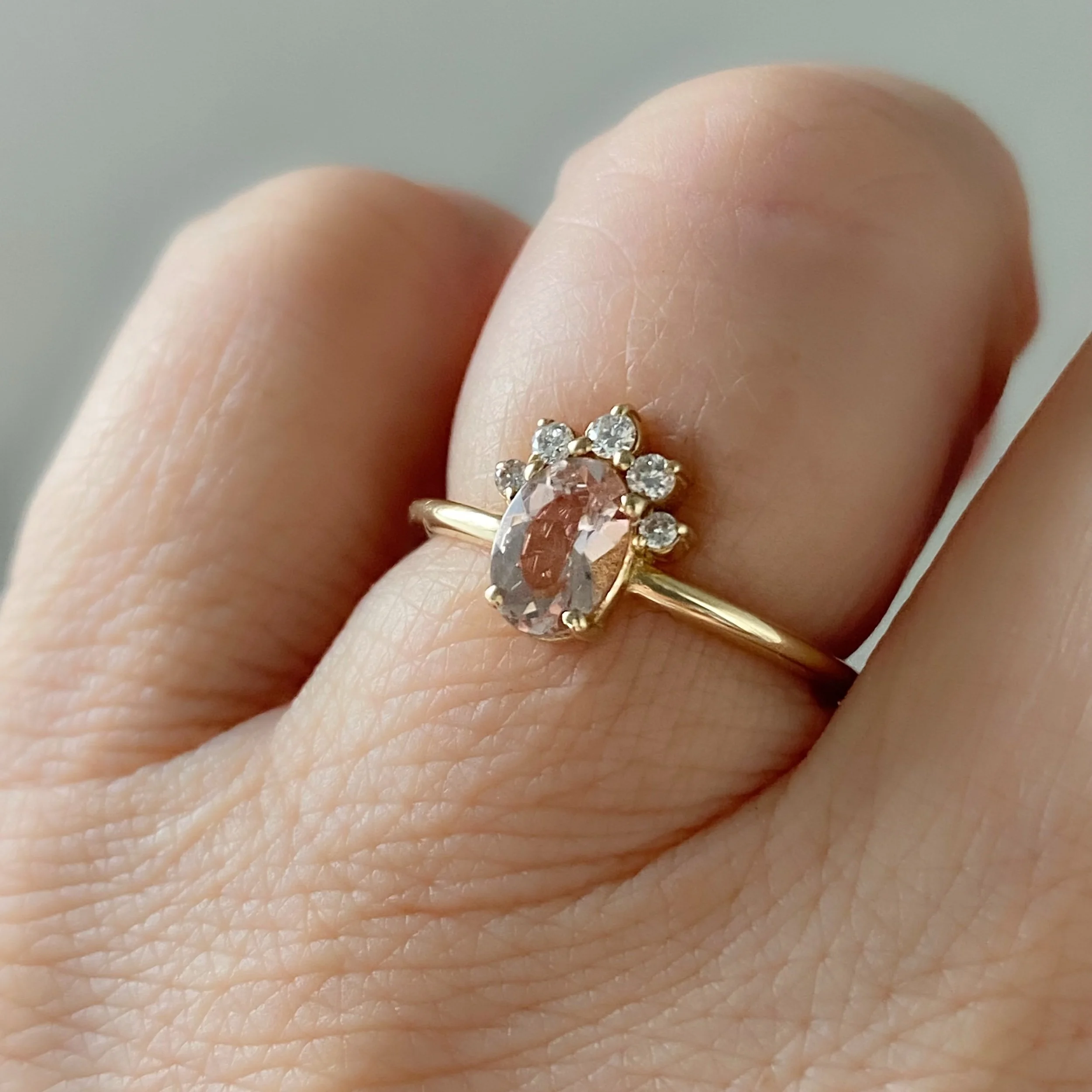 peachy pink oval morganite with little crown of Canadian diamonds claw set in 14k yellow gold narrow rounded band on hand Kim Drosdick Jewellery Toronto