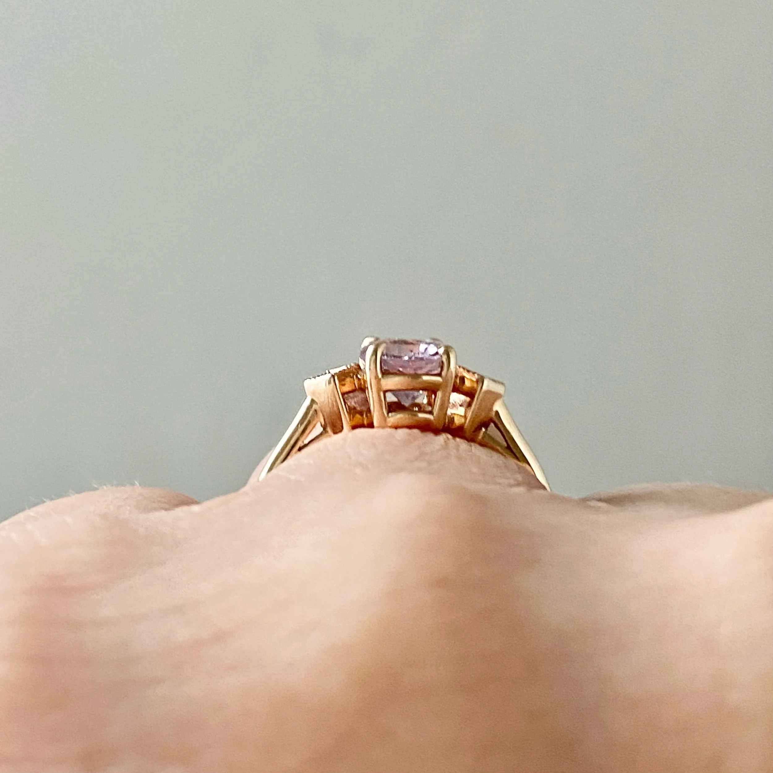 oval pink spinel claw set engagement ring with tilted square bezel set diamonds 14k yellow gold through finger view on hand Kim Drosdick Jewellery Toronto