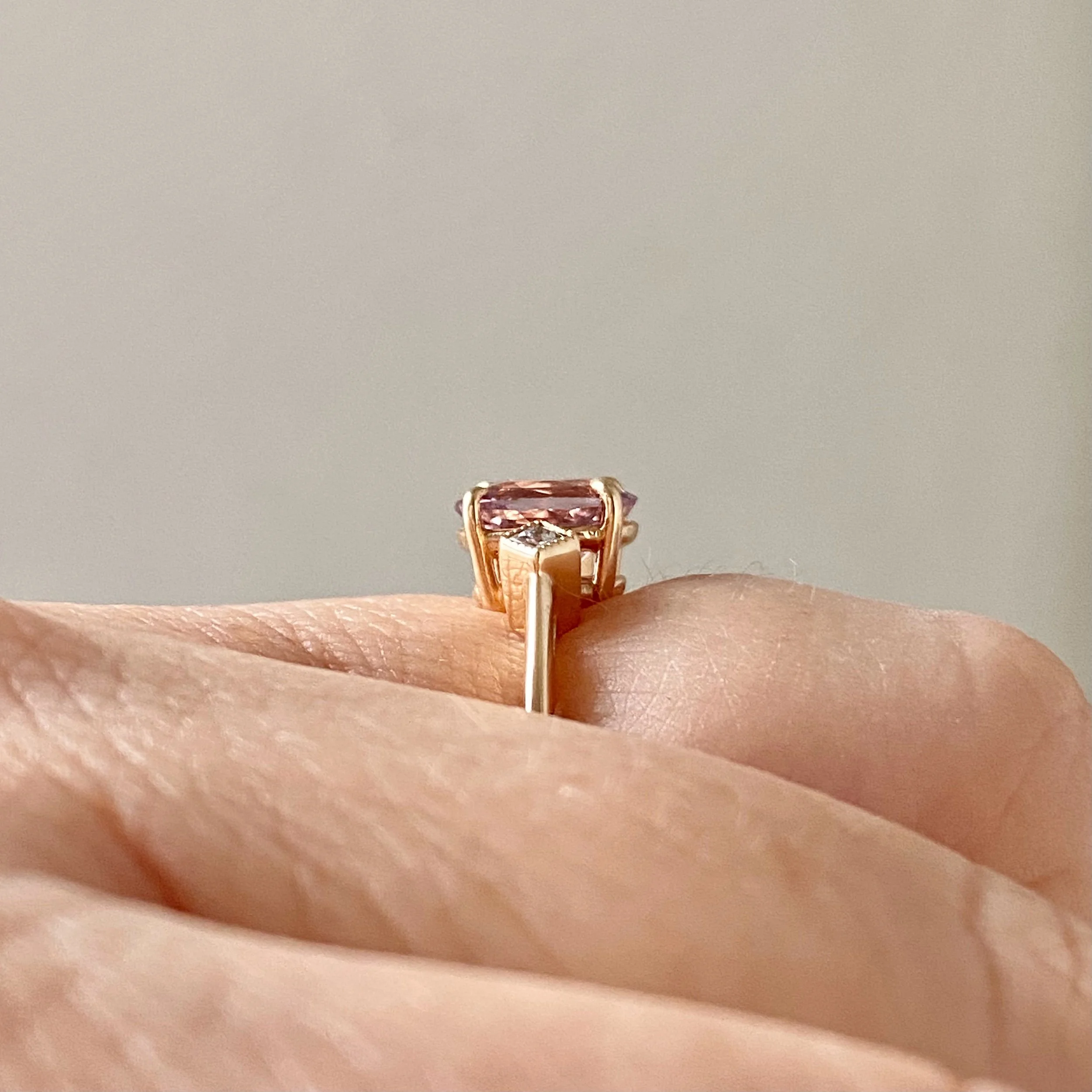 oval pink spinel claw set engagement ring with tilted square bezel set diamonds 14k yellow gold side view on hand Kim Drosdick Jewellery Toronto