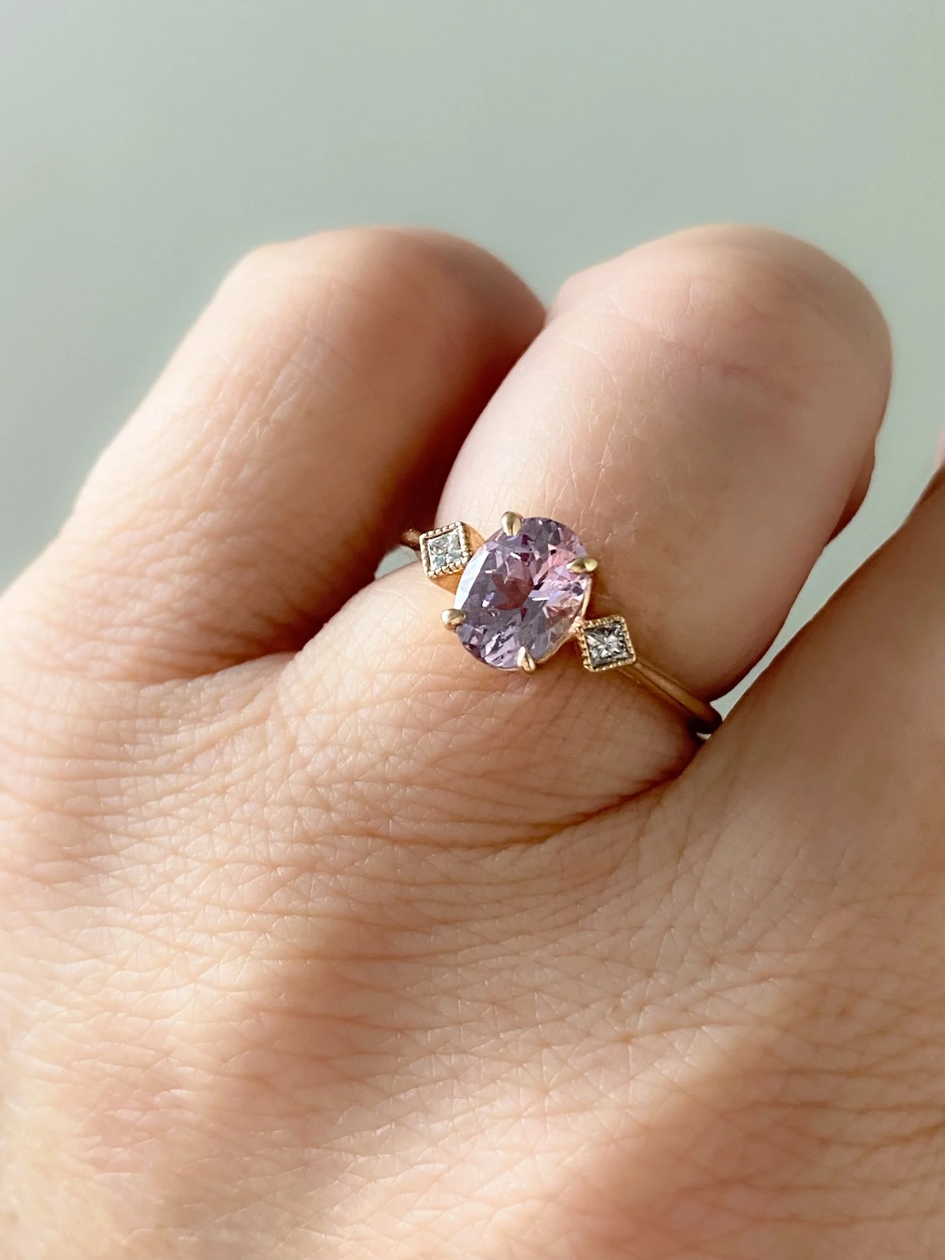 oval pink spinel claw set engagement ring with tilted square bezel set diamonds 14k yellow gold on hand Kim Drosdick Jewellery Toronto
