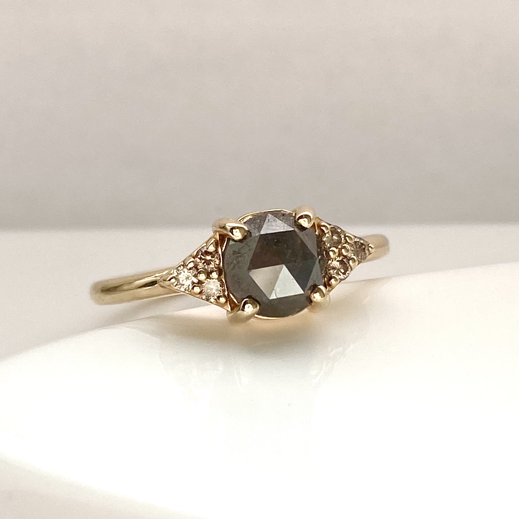 dark grey rose cut diamond engagement ring with diamond trio triangle sides 14k yellow gold front view on prop dish Kim Drosdick Jewellery Toronto