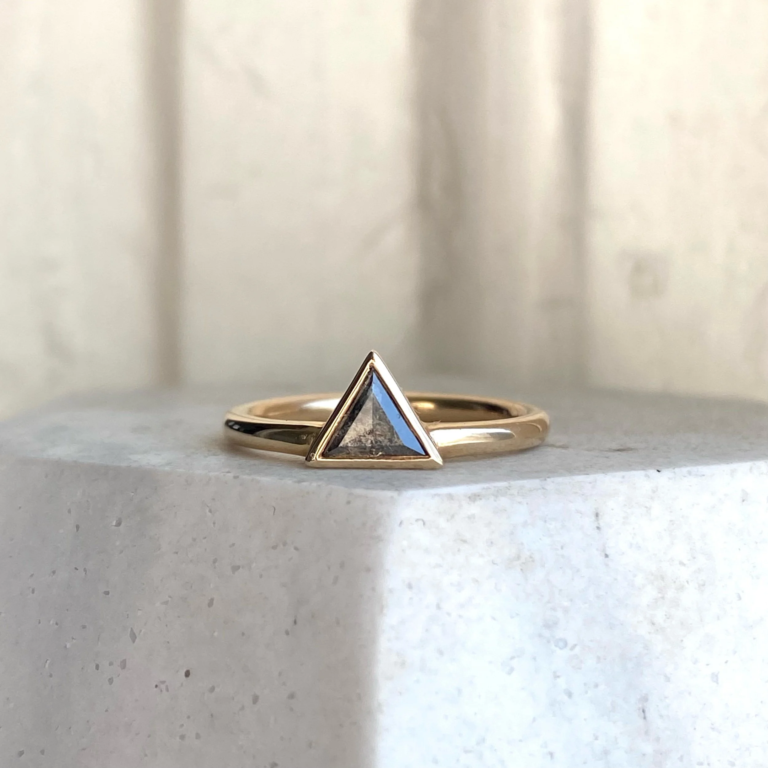 darker triangle salt and pepper diamond bezel set off side bottom justified to round wire band 14k yellow gold front view on prop Kim Drosdick Jewellery Toronto