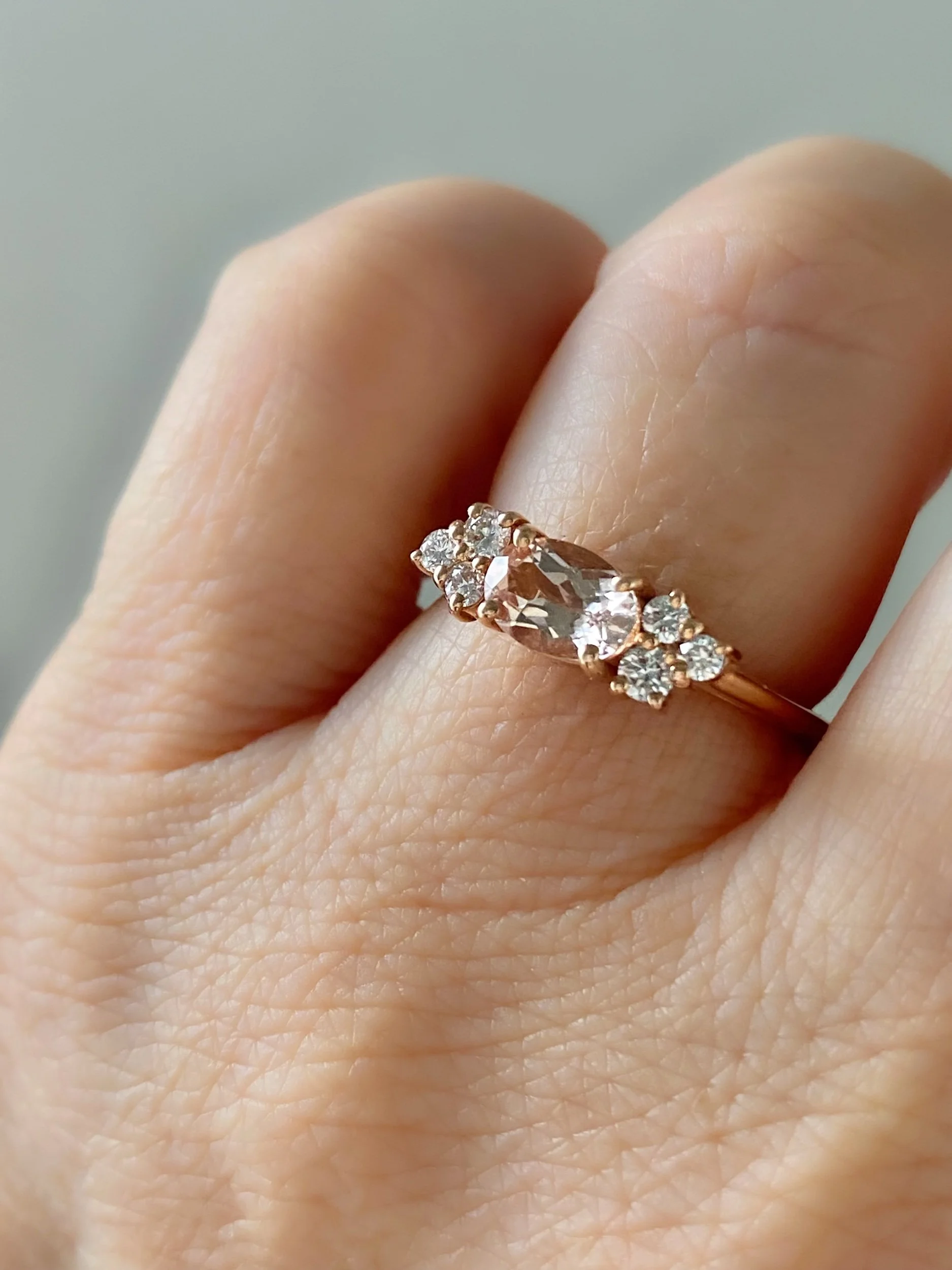 east west claw set oval morganite with mixed size round mirrored canadian diamond clusters shown on hand and raised to allows future flush wedding ring 14k rose gold Kim Drosdick Jewellery Toronto