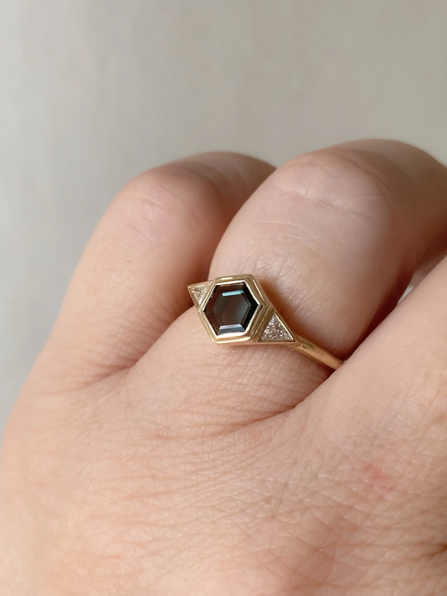 dark teak hexagonal spinel 3 stone engagement ring bezel settings rounded narrow band 14k yellow gold on hand Kim Drosdick Jewellery Toronto