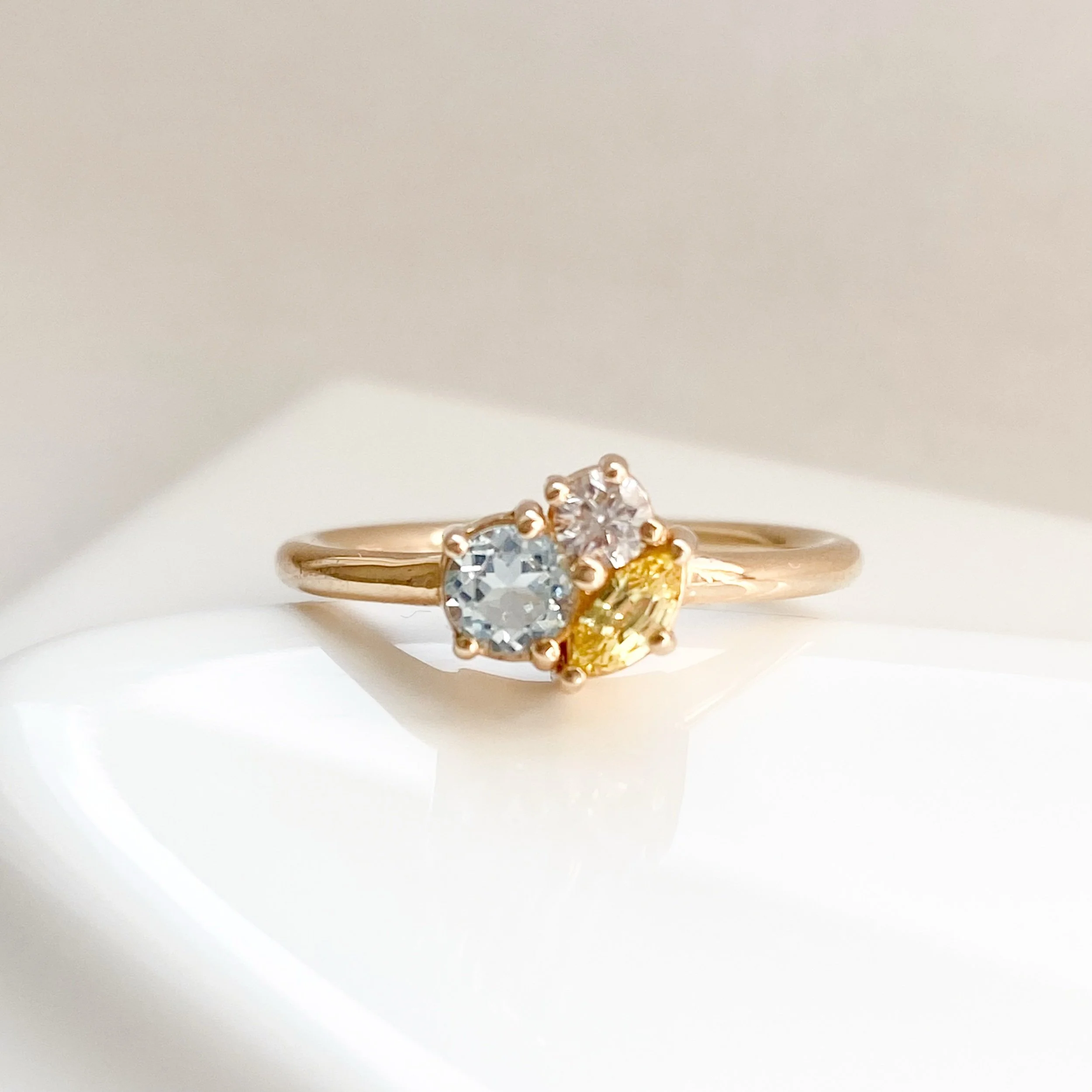 three stone cluster ring in 14k recycled yellow gold using aquamarine diamond and yellow sapphire  sits low to the hand pictured on prop