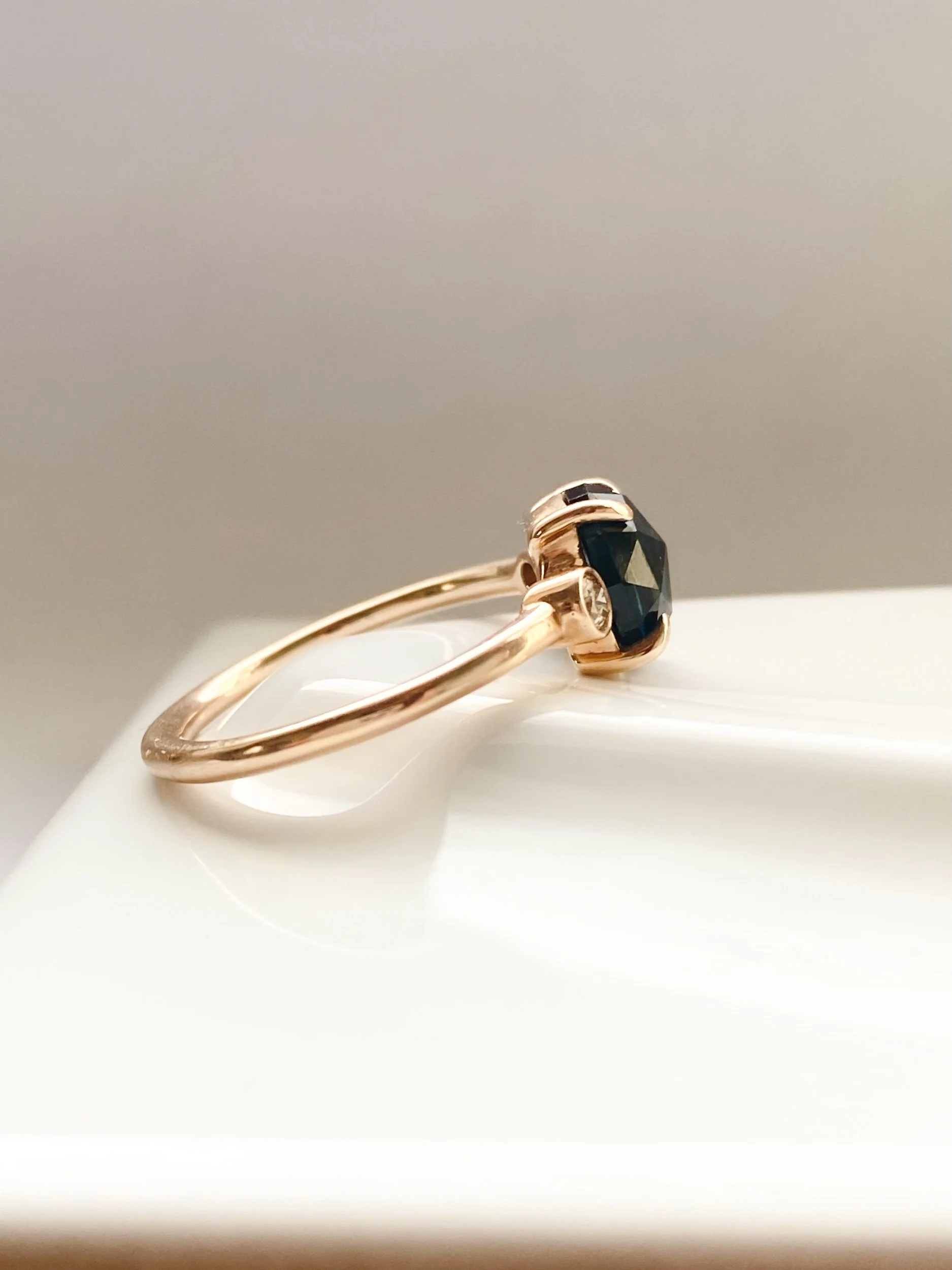 rose cut blue oval sapphire 3-stone champagne diamond alternative engagement ring 14k yellow gold bezel set claw set rounded band Kim Drosdick Jewellery Toronto on dish side view