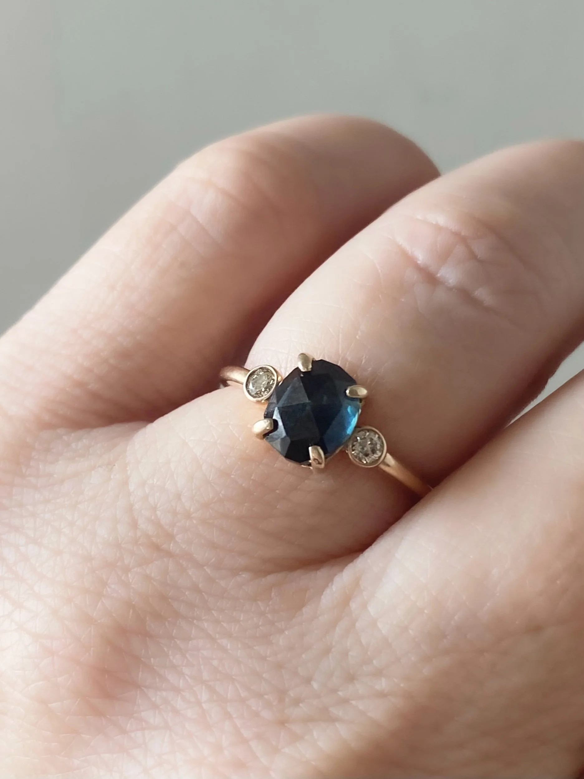rose cut blue oval sapphire 3-stone champagne diamond alternative engagement ring 14k yellow gold bezel set claw set rounded band Kim Drosdick Jewellery Toronto  on hand