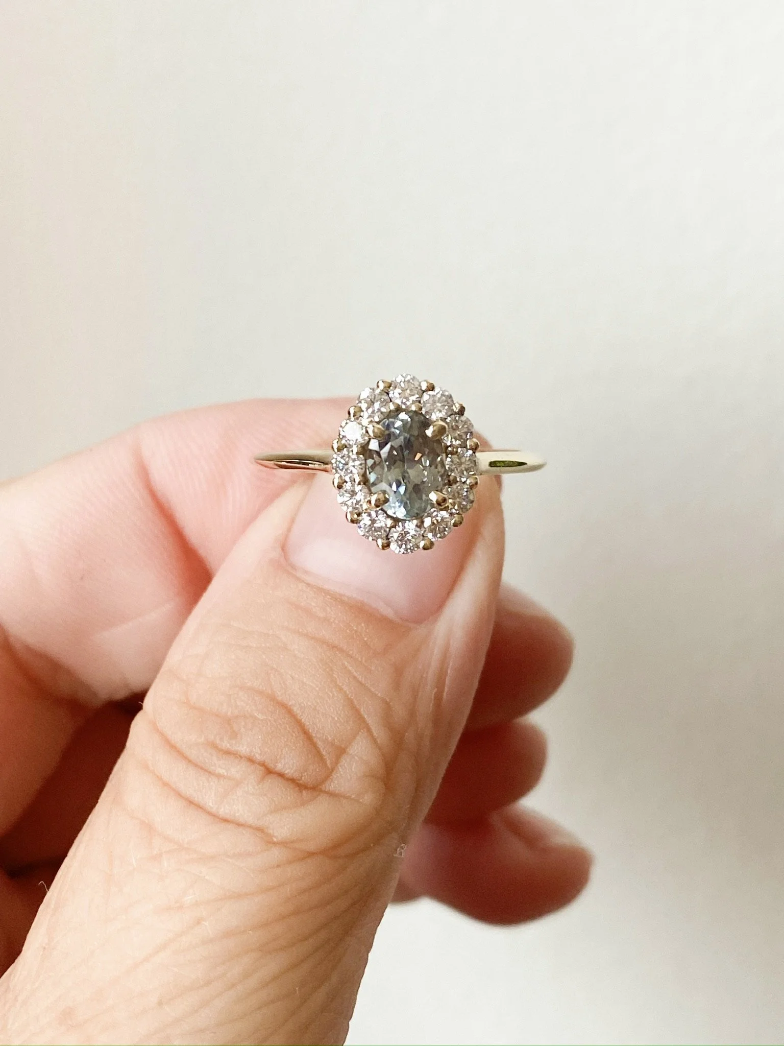 oval blue green spinel claw set in a Canadian diamond halo engagement ring 14k yellow gold side view held by fingers Kim Drosdick Jewellery