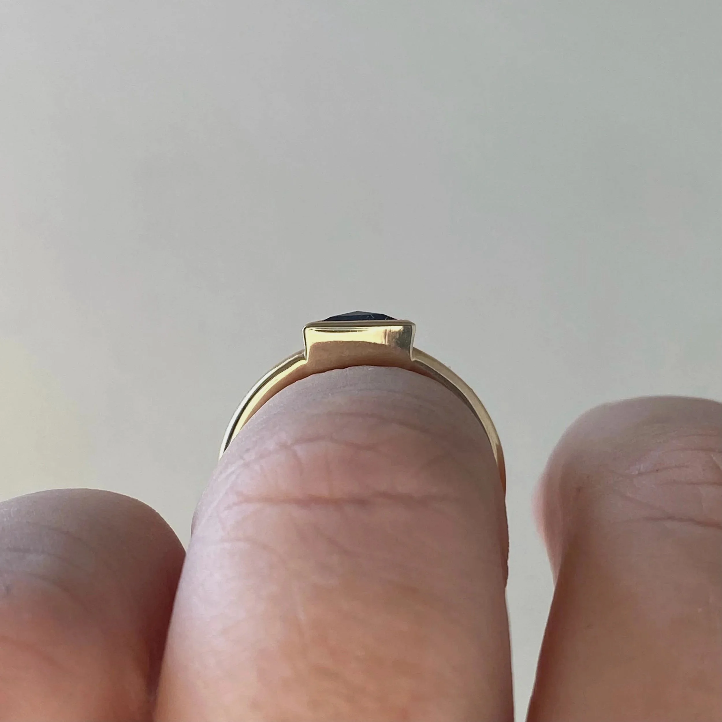 darker triangle salt and pepper diamond bezel set off side bottom justified to round wire band 14k yellow gold through finger view on hand Kim Drosdick Jewellery Toronto