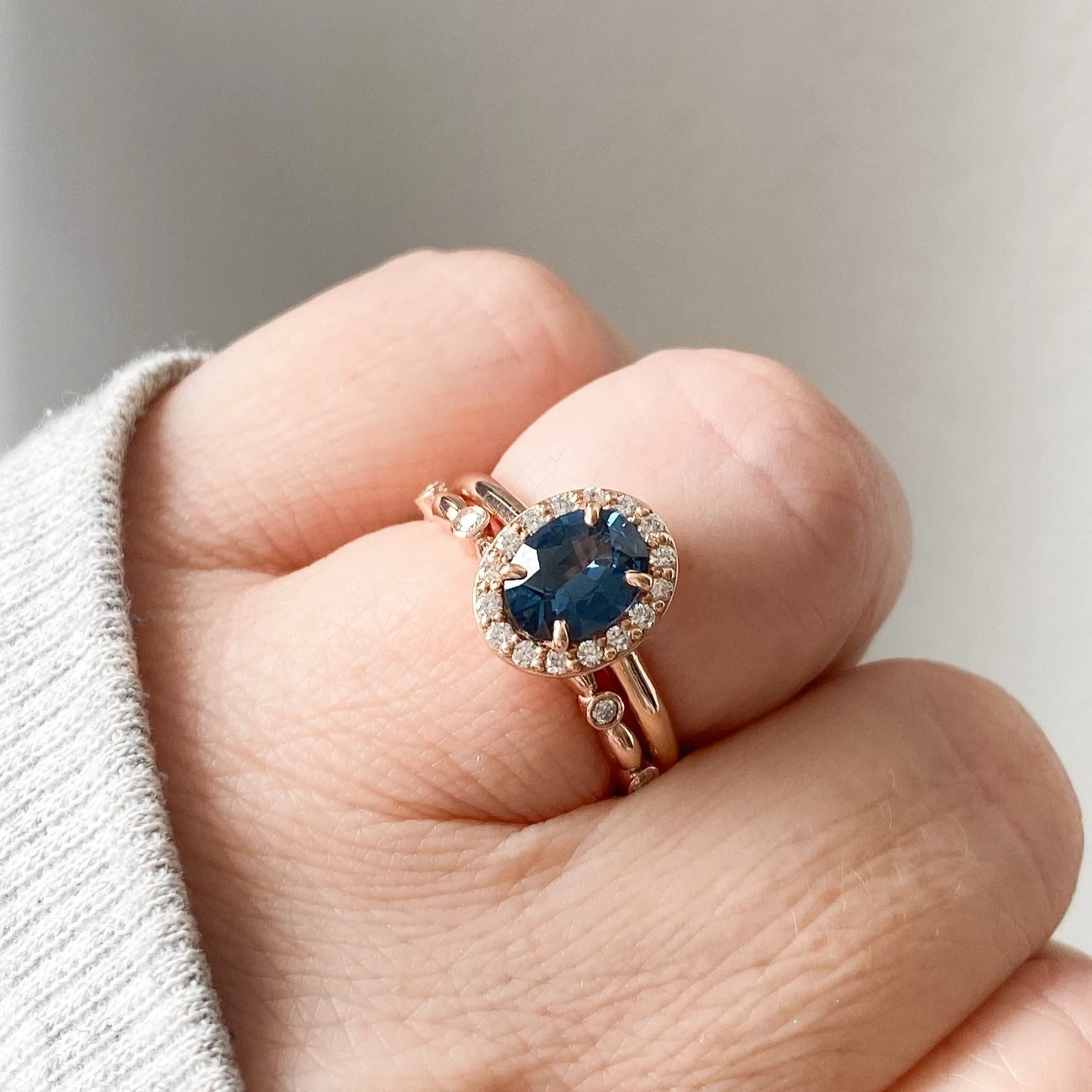 gorgeous oval blue spinel centre stone Canadian diamond halo engagement ring 14k rose gold on hand with companion wedding ring Kim Drosdick Jewellery