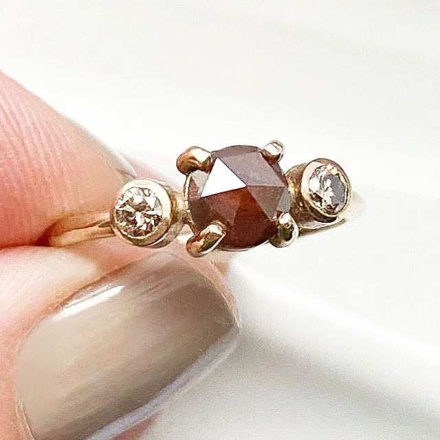round deep red rose cut claw set diamond flanked by bezel set champagne brilliant cut diamonds 14k yellow gold in between fingers Kim Drosdick Jewellery Toronto