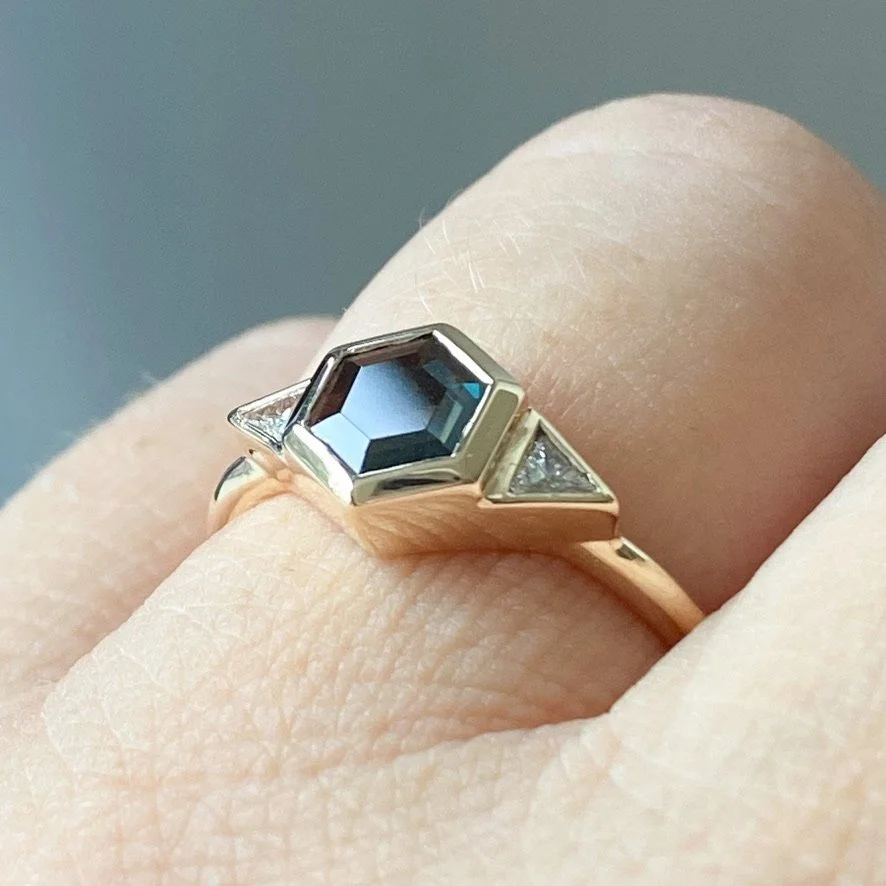 dark teak hexagonal spinel 3 stone engagement ring bezel settings rounded narrow band 14k yellow gold on hand Kim Drosdick Jewellery Toronto