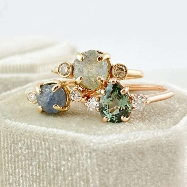 round Montana minty blue green claw set engagement ring with side bezel set champagne diamonds 14k yellow gold front view with 2 other earthy sapphire rings Kim Drosdick Jewellery Toronto