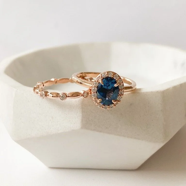 gorgeous oval blue spinel centre stone Canadian diamond halo engagement ring 14k rose gold on hand with companion wedding ring on prop Kim Drosdick Jewellery