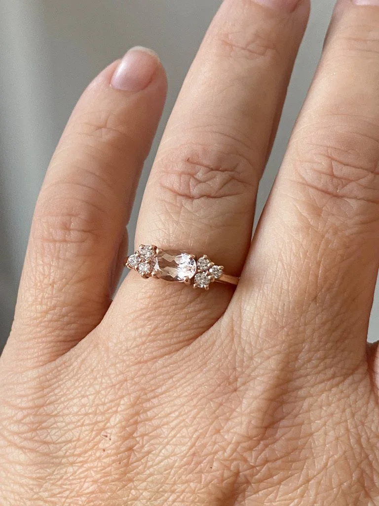 east west claw set oval morganite with mixed size round mirrored canadian diamond clusters shown on hand and raised to allows future flush wedding ring 14k rose gold Kim Drosdick Jewellery Toronto