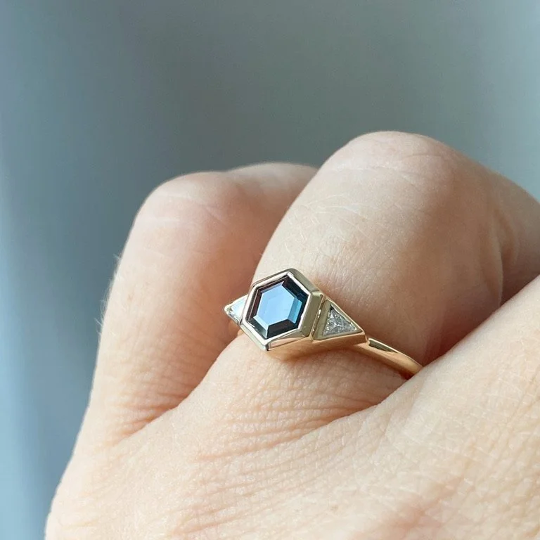 dark teak hexagonal spinel 3 stone engagement ring bezel settings rounded narrow band 14k yellow gold alt on hand Kim Drosdick Jewellery Toronto