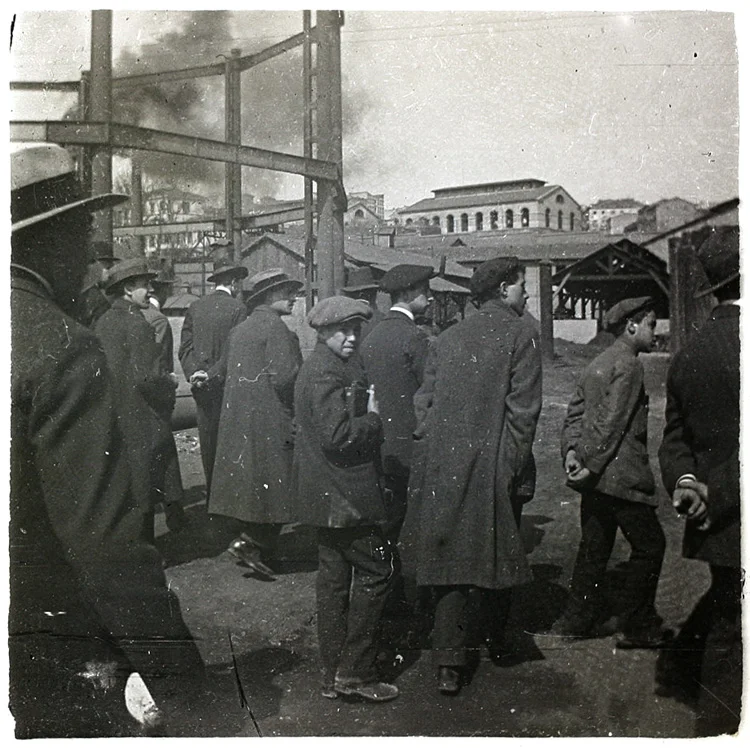 Obreros madrileños en 1920. Hombres y niños con abrigo, boina y sombreros entrando a la fábrica. Fragmento de placa esterescópica. Foto: Cano.